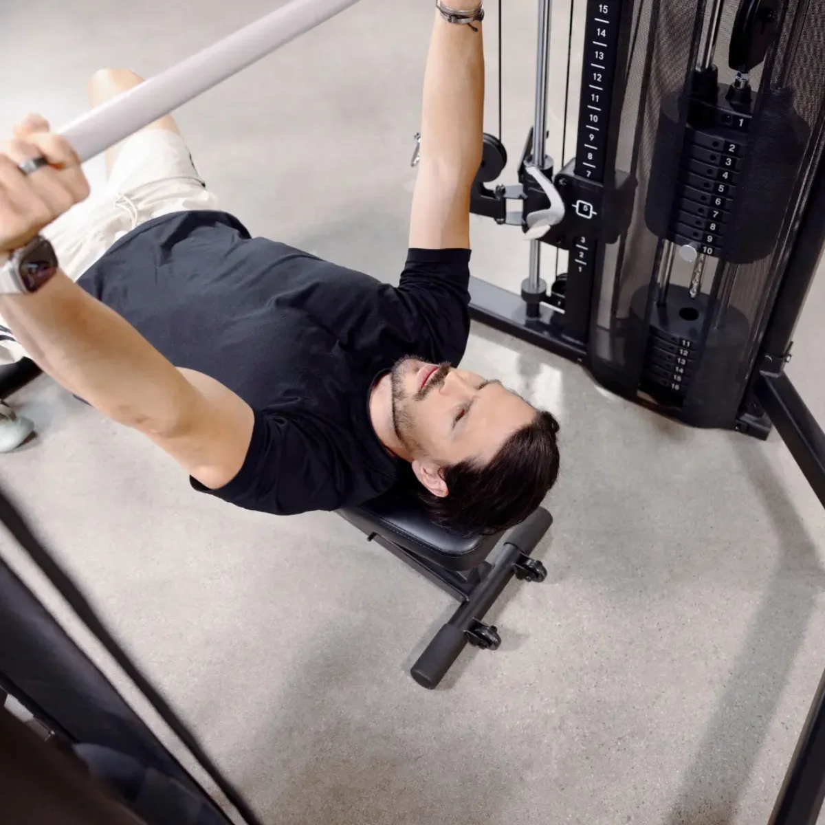 Mann liegt auf einer Hantelbank und hebt eine Stange in einem Fitnessstudio.