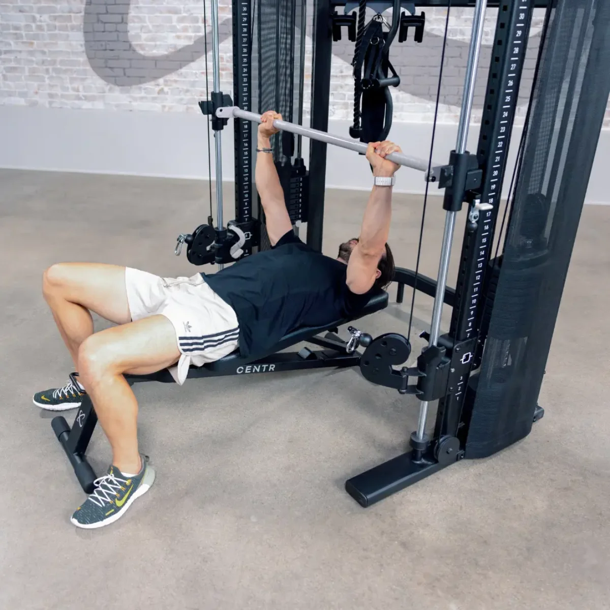 Mann trainiert an einer Fitnessmaschine und macht Bankdrücken. Grauer Hintergrund.