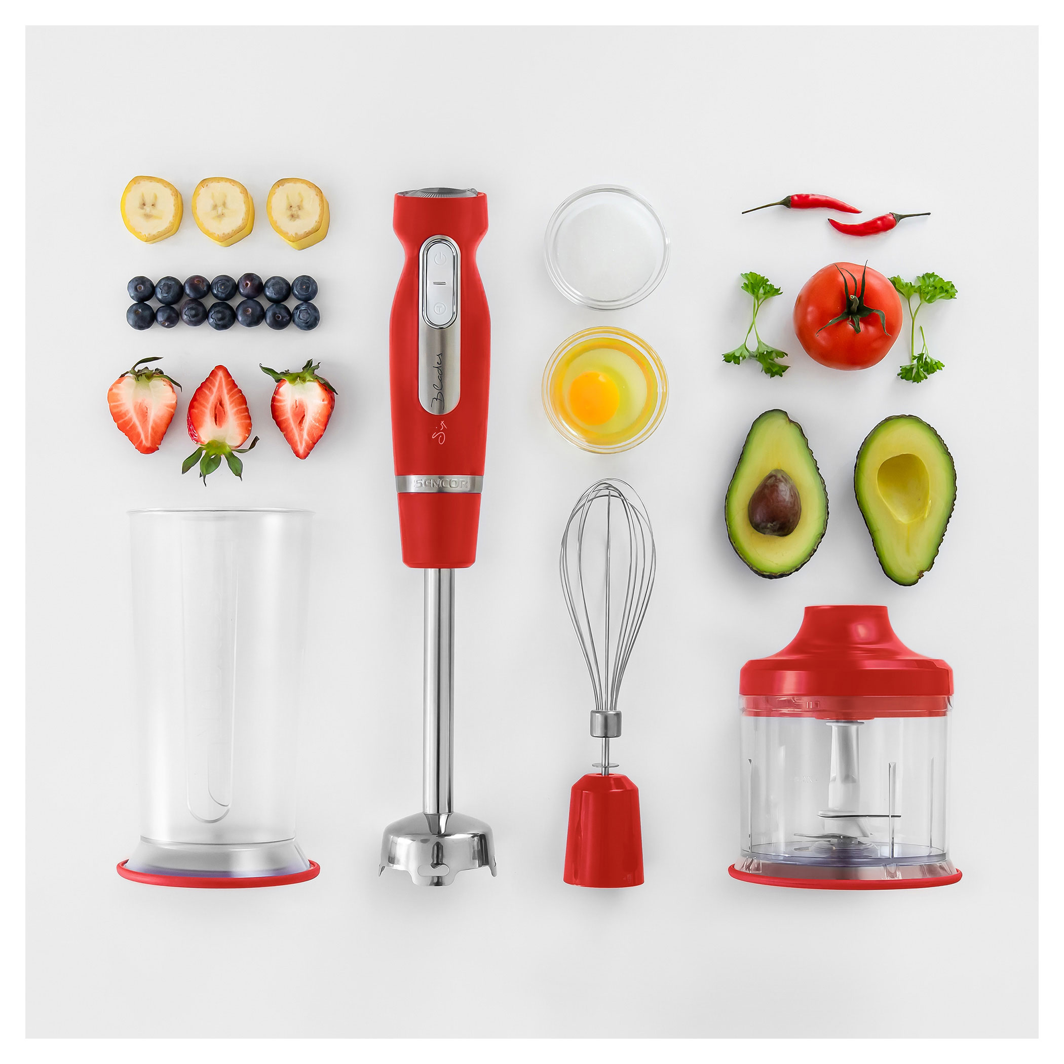 Un frullatore a immersione rosso con vari ingredienti: banane, mirtilli, fragole, pomodori, avocado e uova.