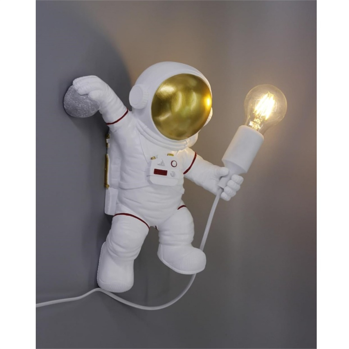 Astronaut-Wandlampe, die eine Glühbirne hält. Weißer Anzug mit goldenem Gesicht, graue Wand.