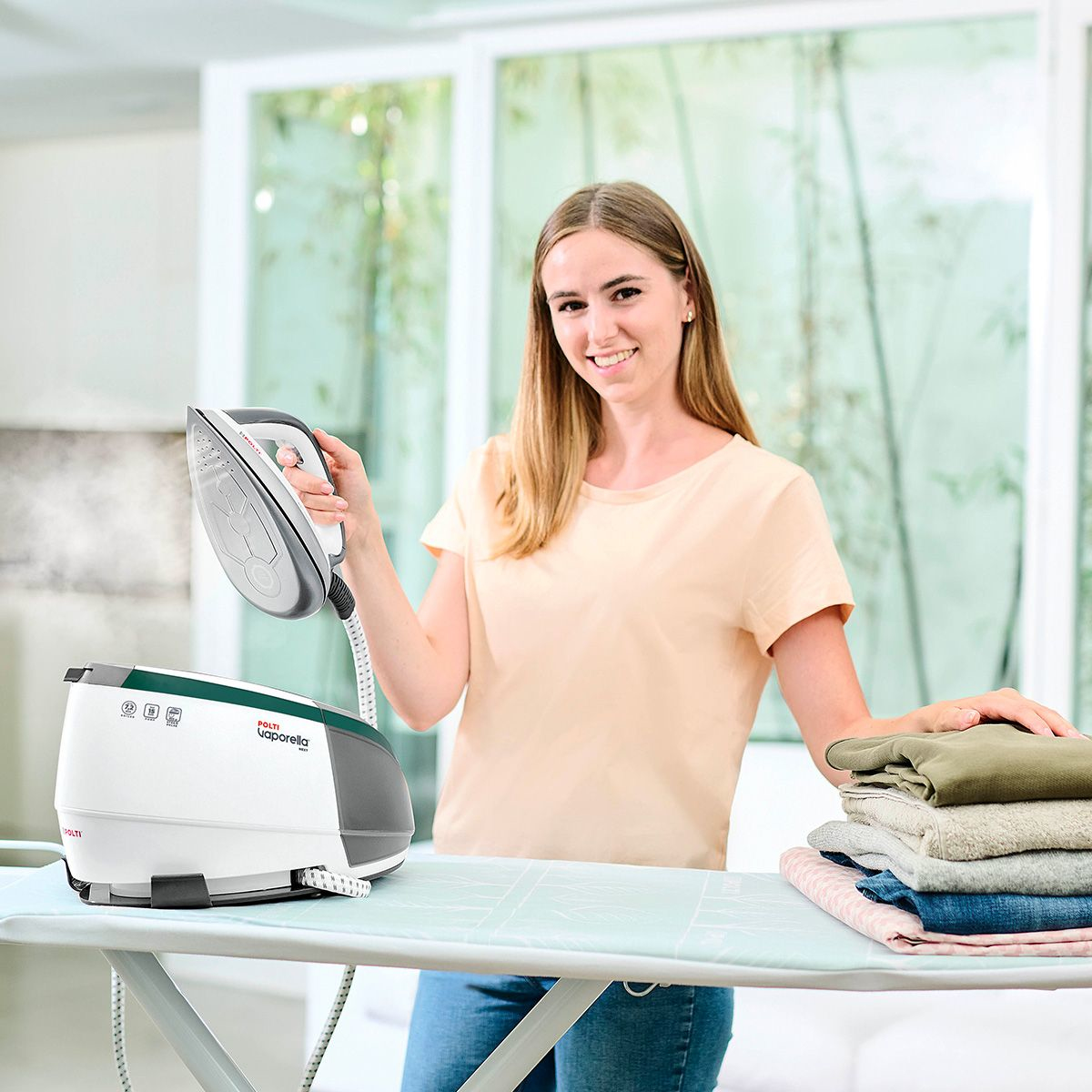 Frau bügelt Kleidung mit Dampfbügeleisen und Dampfgenerator, lächelt.