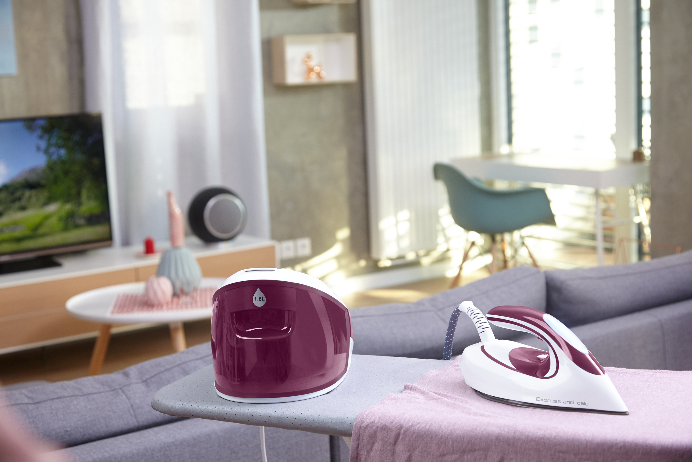 Ein Wohnzimmer mit einem Bügeleisen auf einem Bügelbrett und einem Sofa im Hintergrund.