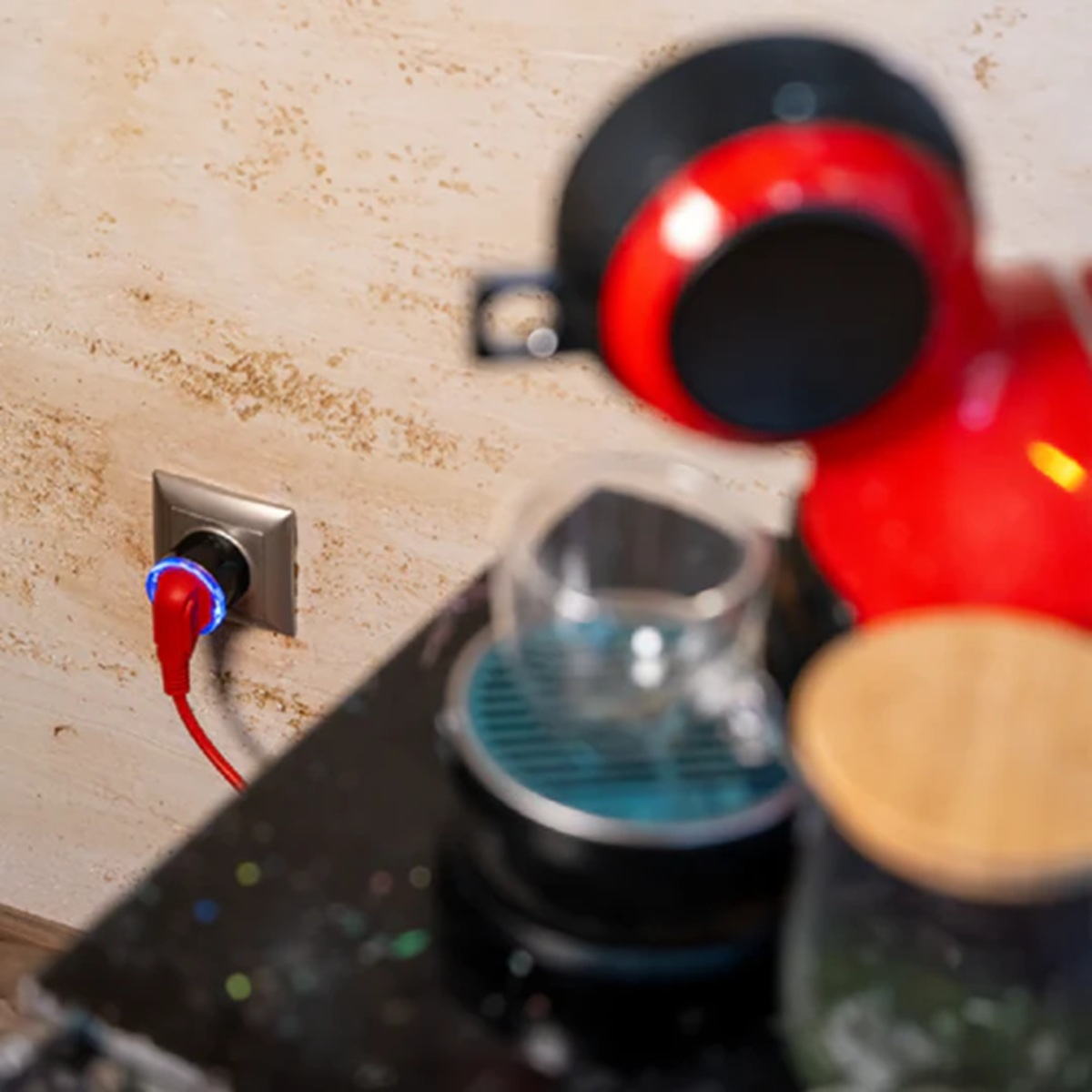 Czerwony ekspres do kawy podłączony do gniazdka ściennego, z filiżanką obok.