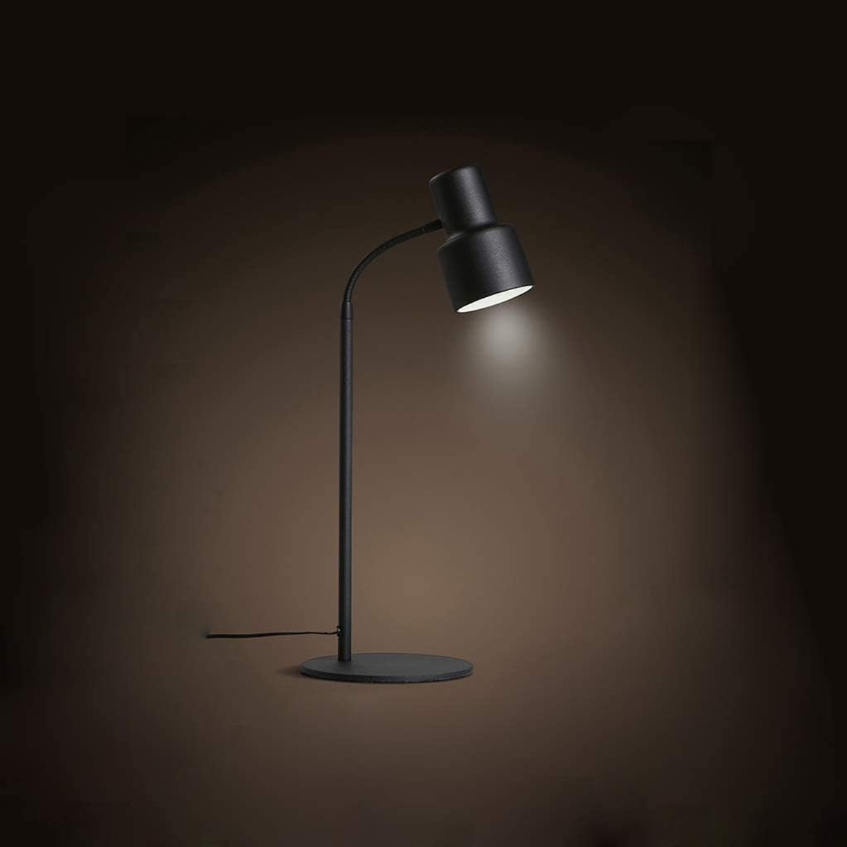 Czarna lampa biurkowa z zakrzywionym ramieniem, świecąca światłem na ciemne tło.