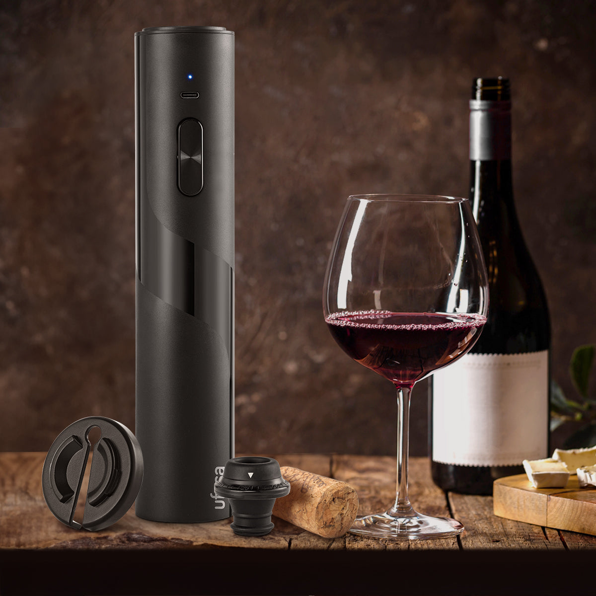 Una bottiglia di vino, un bicchiere di vino rosso e un cavatappi. C'è un tappo e formaggio su un tavolo.