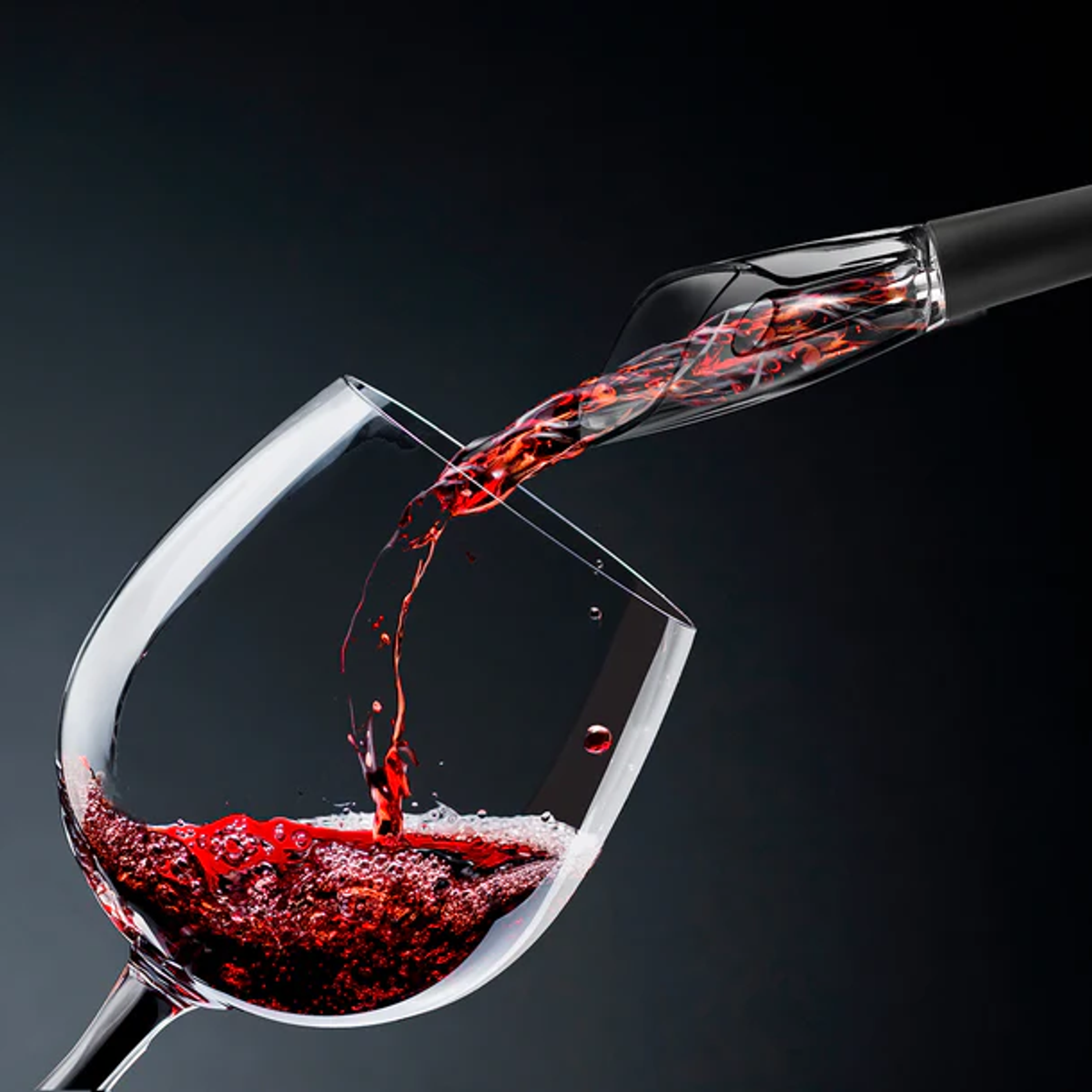 Vino tinto que se vierte en una copa desde un aireador negro. Fondo oscuro, la copa está llena.