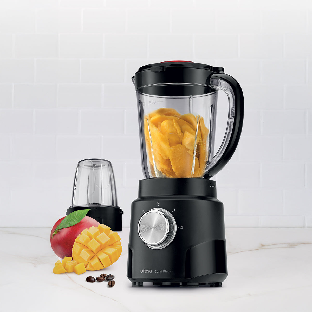 Licuadora negra llena de trozos de mango amarillo. Mango, semillas y vaso de licuadora adicionales presentes.