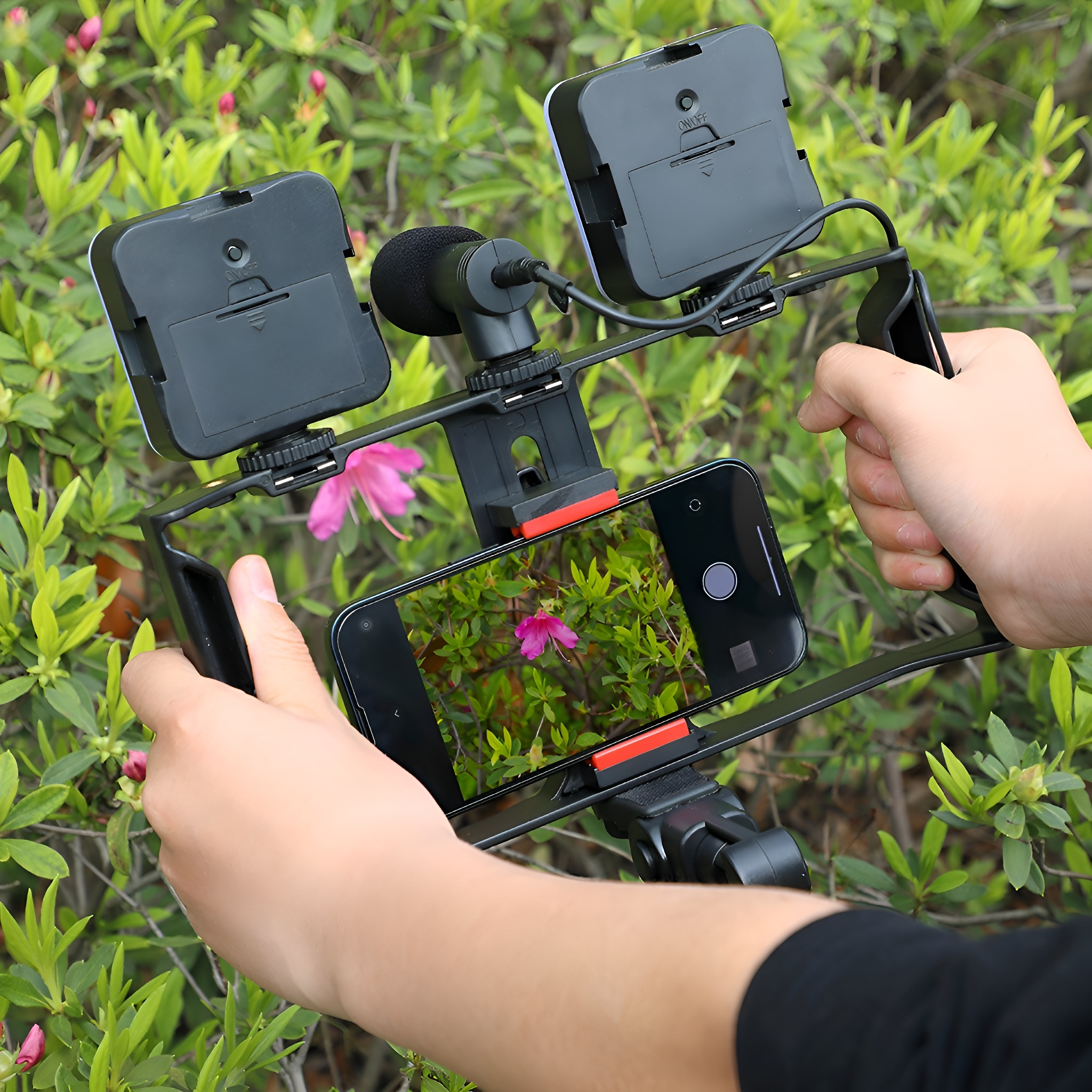 Zwei Hände halten ein Telefon mit Filmausrüstung. Das Telefon zeigt Blumen. Grünes Laub umgibt.