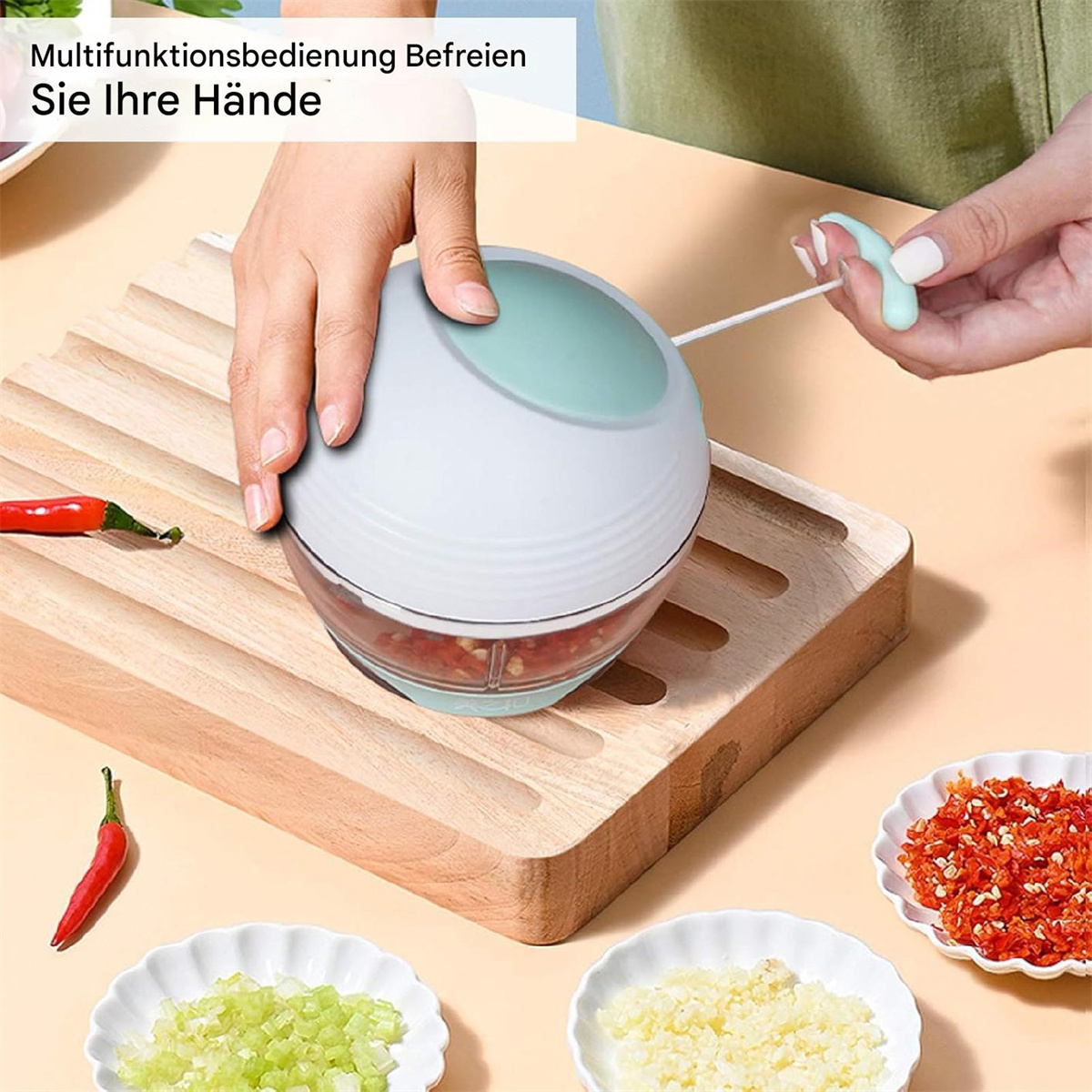 Die Hand einer Person bedient einen manuellen Zerkleinerer mit Zutaten wie Chili und Knoblauch in der Nähe.