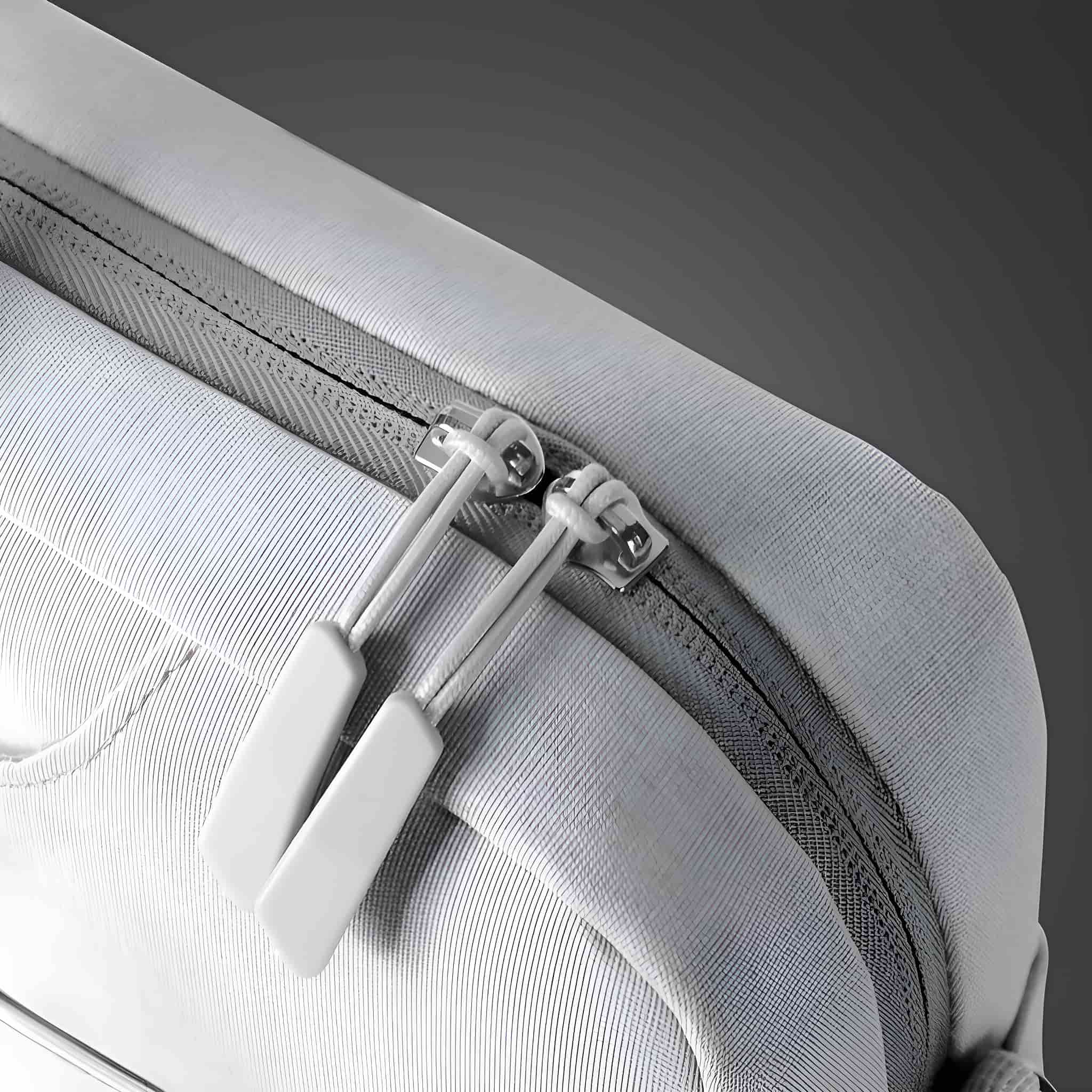 Nahaufnahme eines hellgrauen Reißverschlusses mit weißen Zipper-Anhängern auf grauer Stoffoberfläche.