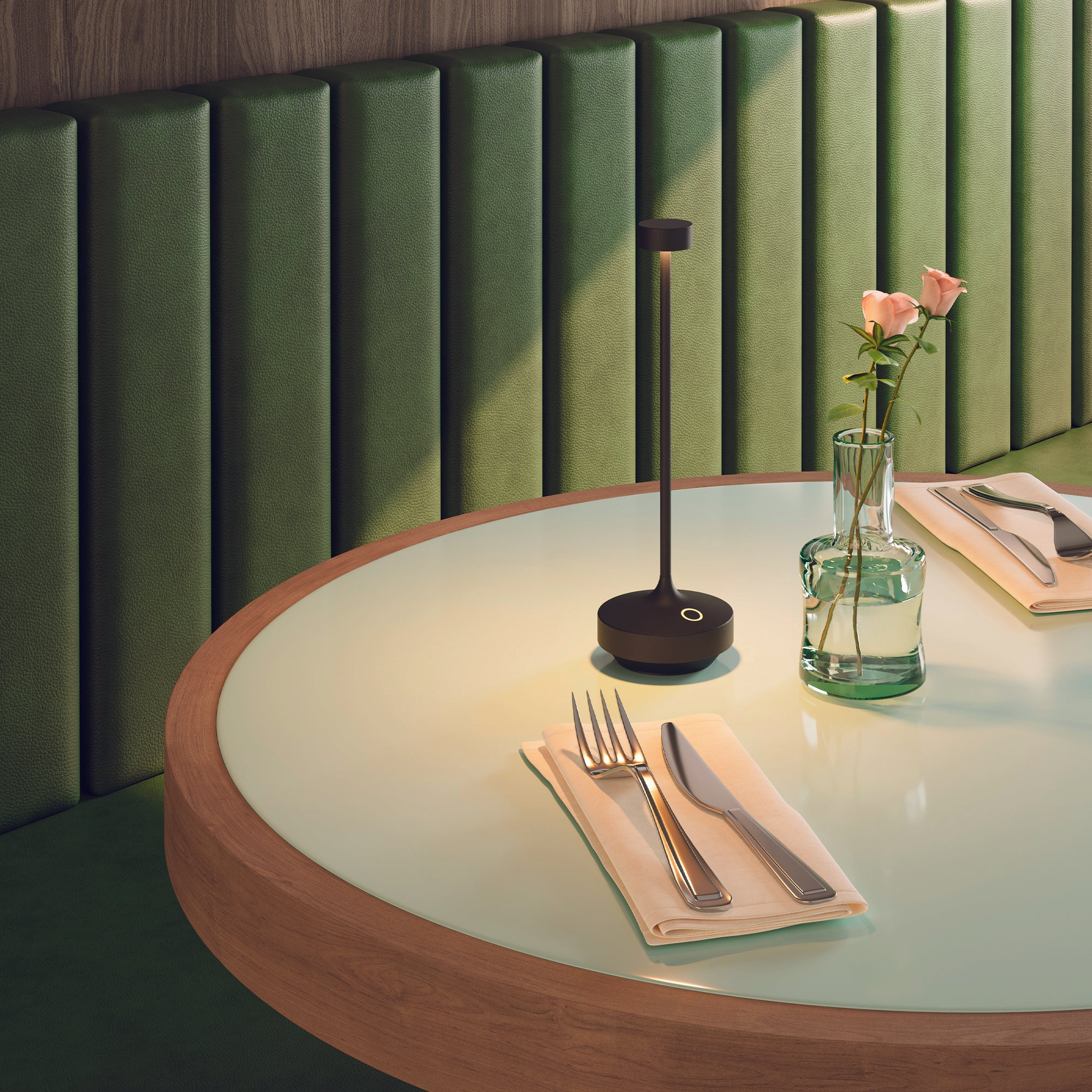 Tisch mit Lampe, Blumen und Besteck. Grüner Tisch mit Holzkante und gepolsterter grüner Wand.