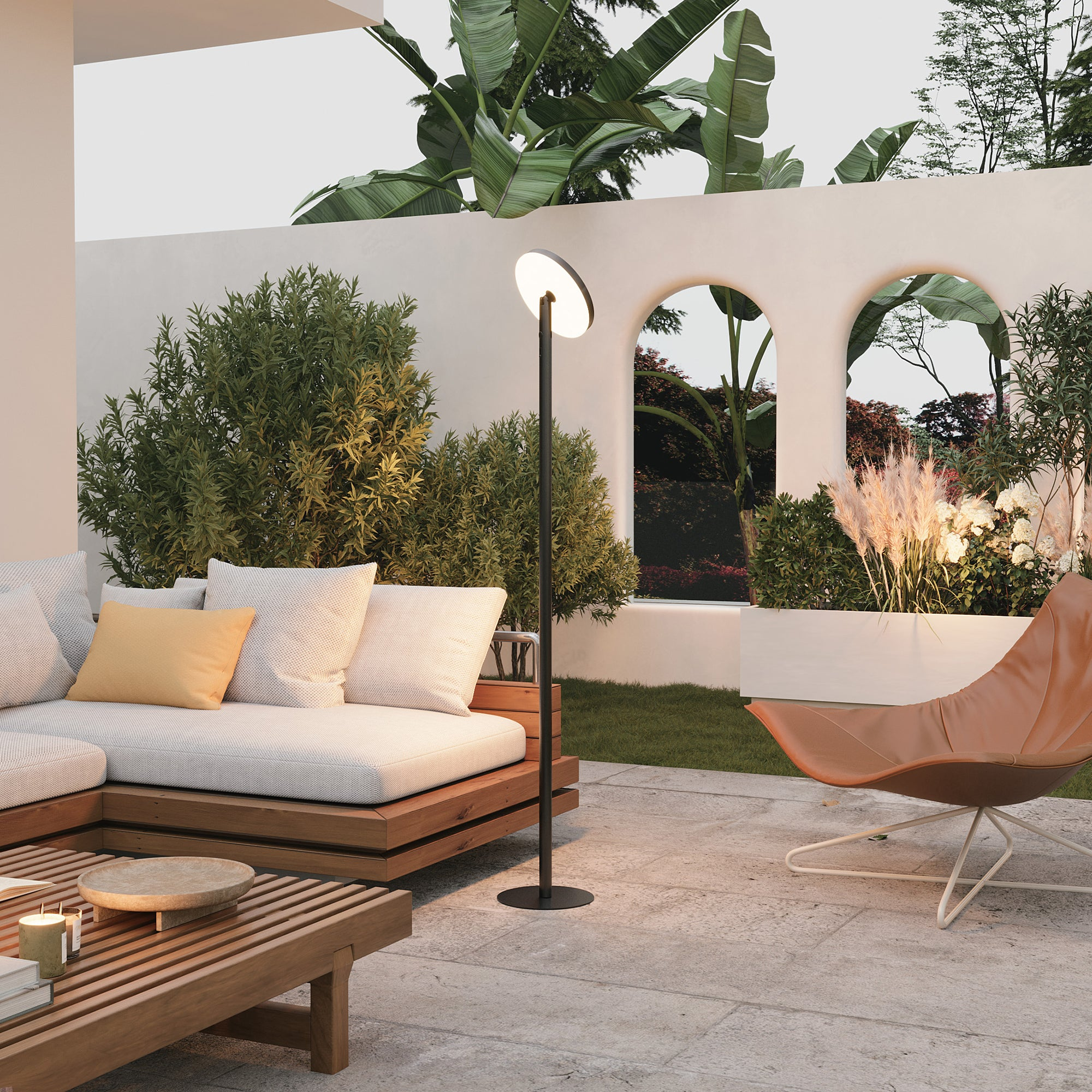 Außenterrasse mit Sofa, Stehlampe, Liegestuhl und üppigem Grün.
