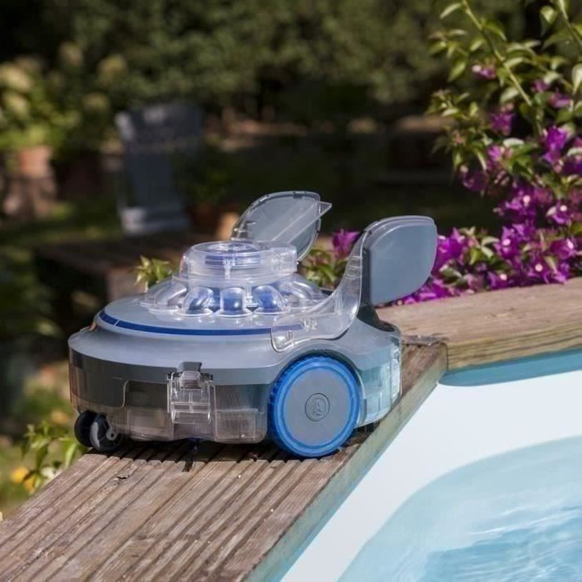 Robot limpiador de piscina sobre madera, cerca de la piscina. Tapa transparente, detalles azules, ruedas y solapas abiertas.