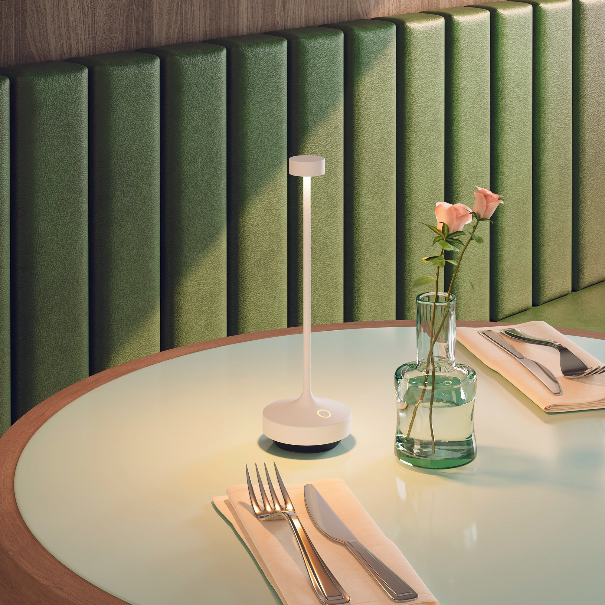 Tisch mit Lampe, Blumen in Vase und Besteck. Grüner Wandhintergrund.