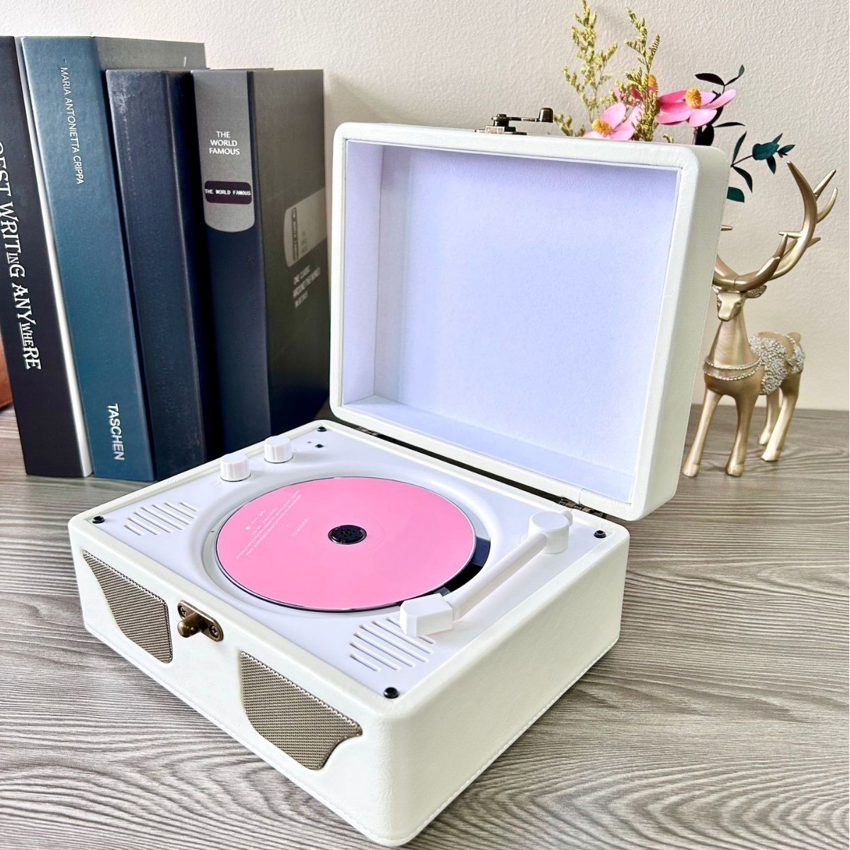 Weißer Vintage-Plattenspieler mit einer rosa Schallplatte, geöffnet auf einem Tisch mit Büchern und Dekoration.
