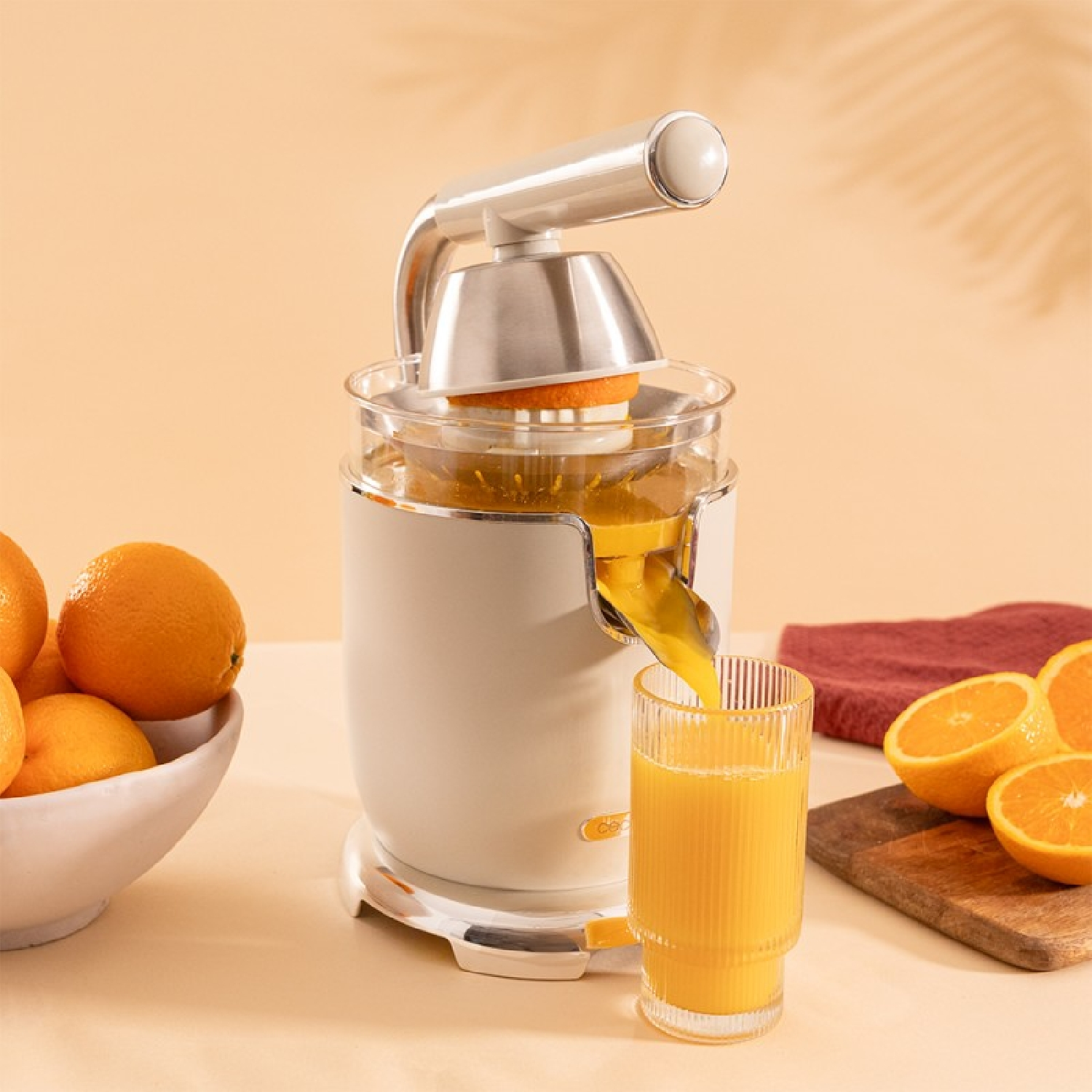 Una exprimidora de naranjas con una naranja y un vaso de jugo. El fondo es naranja claro.