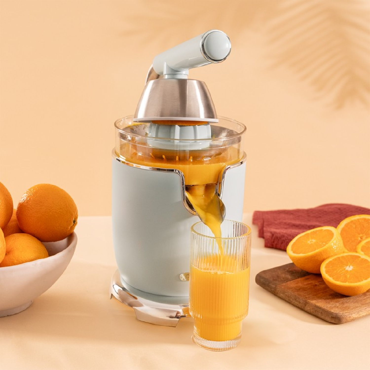 Una exprimidora en acción, con un vaso de zumo y naranjas a la vista.