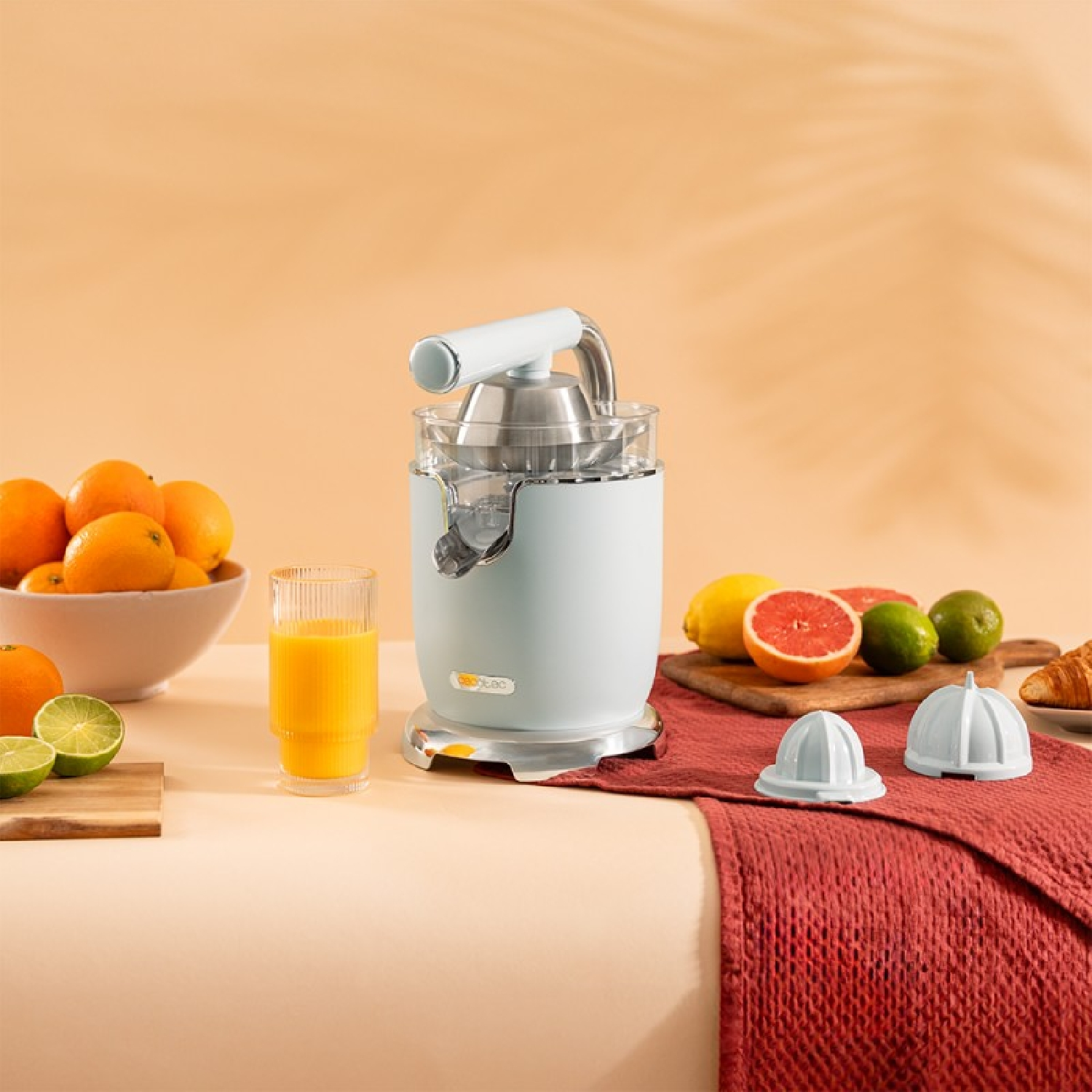 Una exprimidora con naranjas, limas y limones. Se ve un vaso de zumo y otros accesorios.