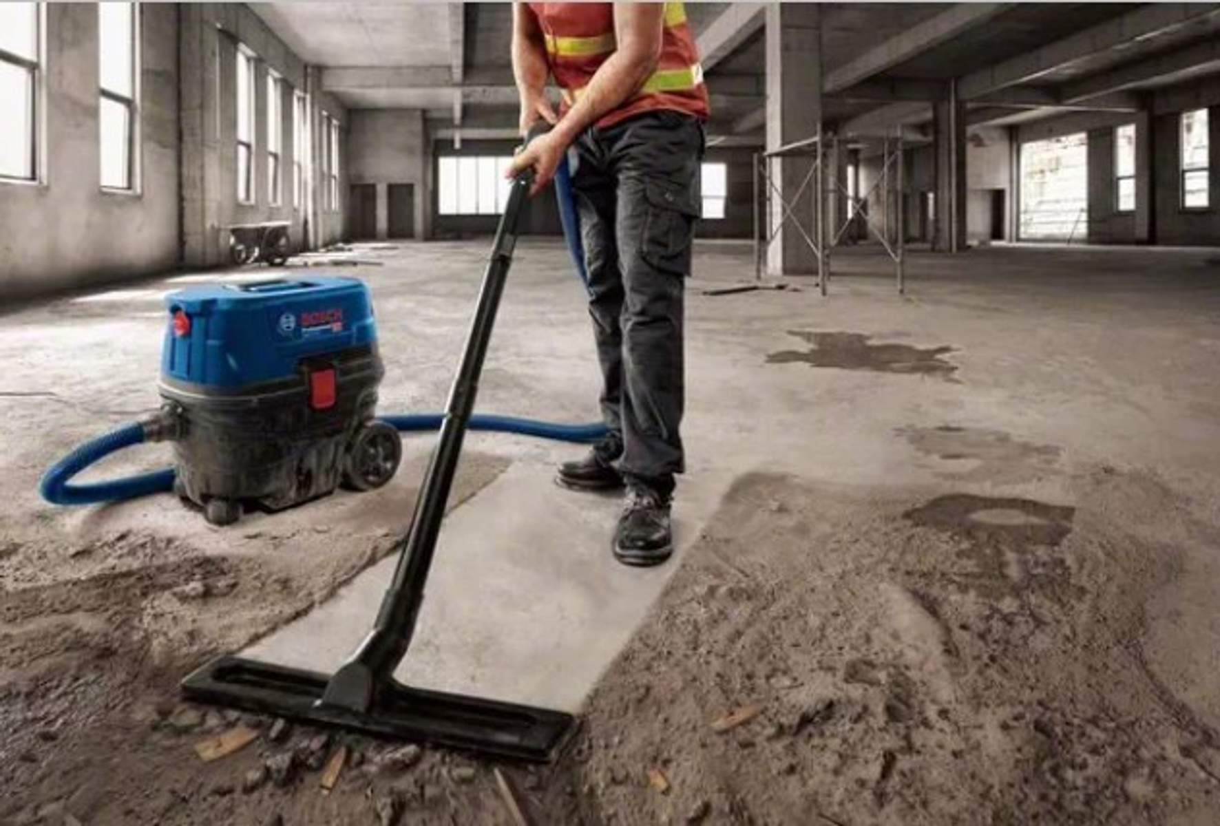 Un operaio aspira un pavimento in cemento in un edificio incompiuto con un aspirapolvere Bosch.