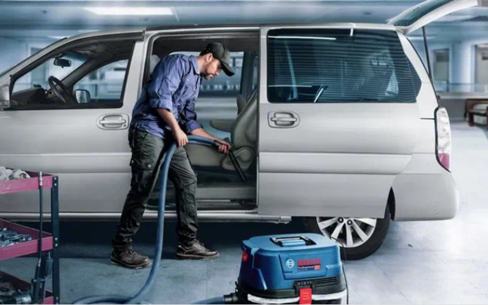 Uomo aspira l'interno di un'auto con un aspirapolvere Bosch blu.