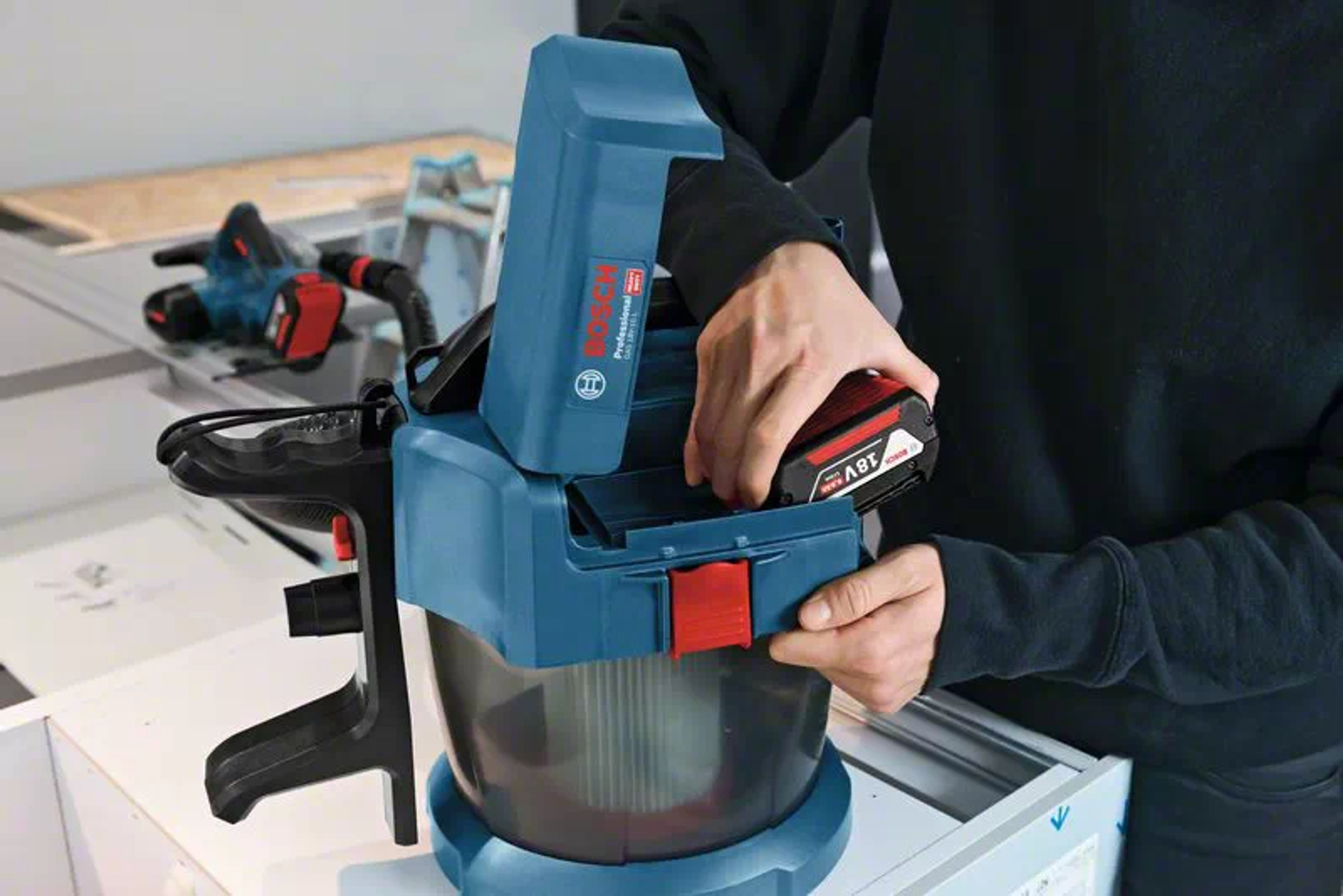 Persona che inserisce la batteria in un aspirapolvere. Blu e nero.
