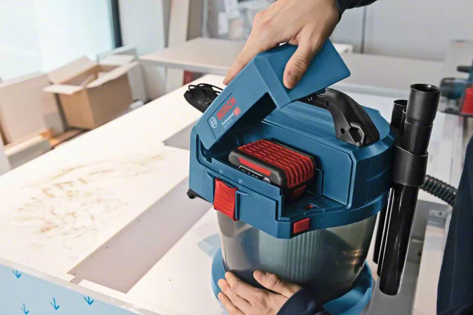 Mani che aprono un aspirapolvere blu, rivelando una batteria.