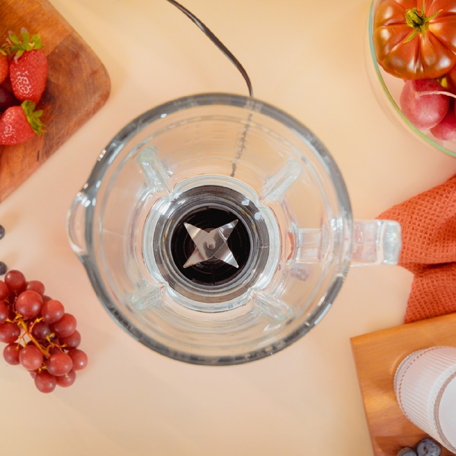 Vista superior de una licuadora con frutas: fresas, uvas y tomates. La licuadora tiene un vaso de vidrio.