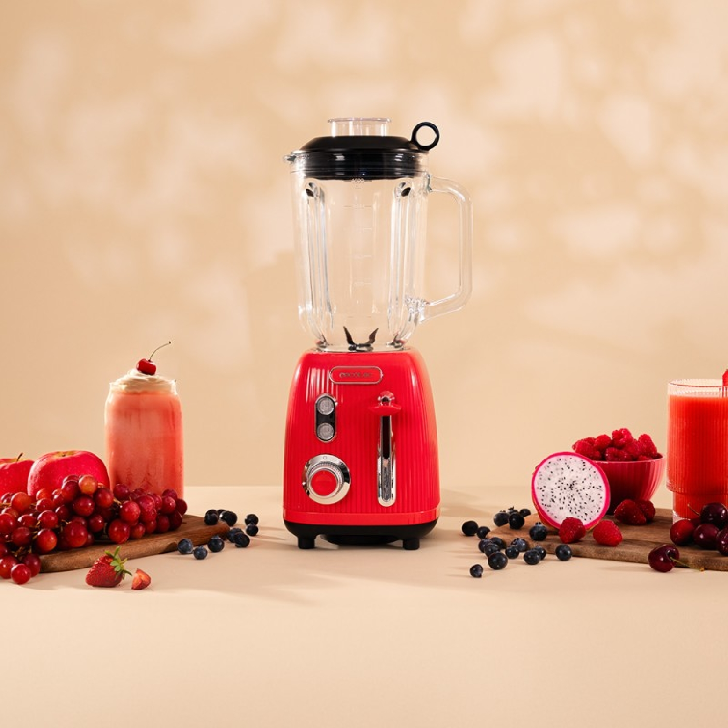 Frullatore rosso con frutta: bacche, uva, frutto del drago e un frullato. Sfondo beige.