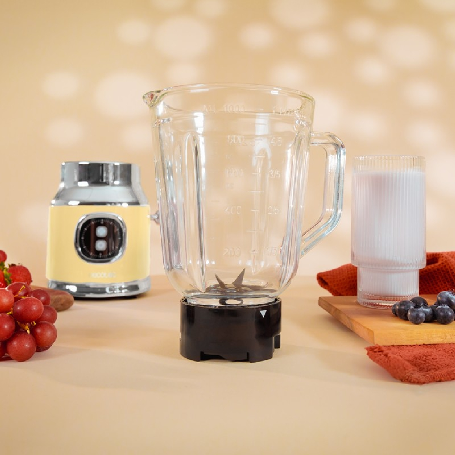 Una licuadora con un vaso de vidrio, una licuadora retro amarilla, un vaso de leche y frutas en una mesa.