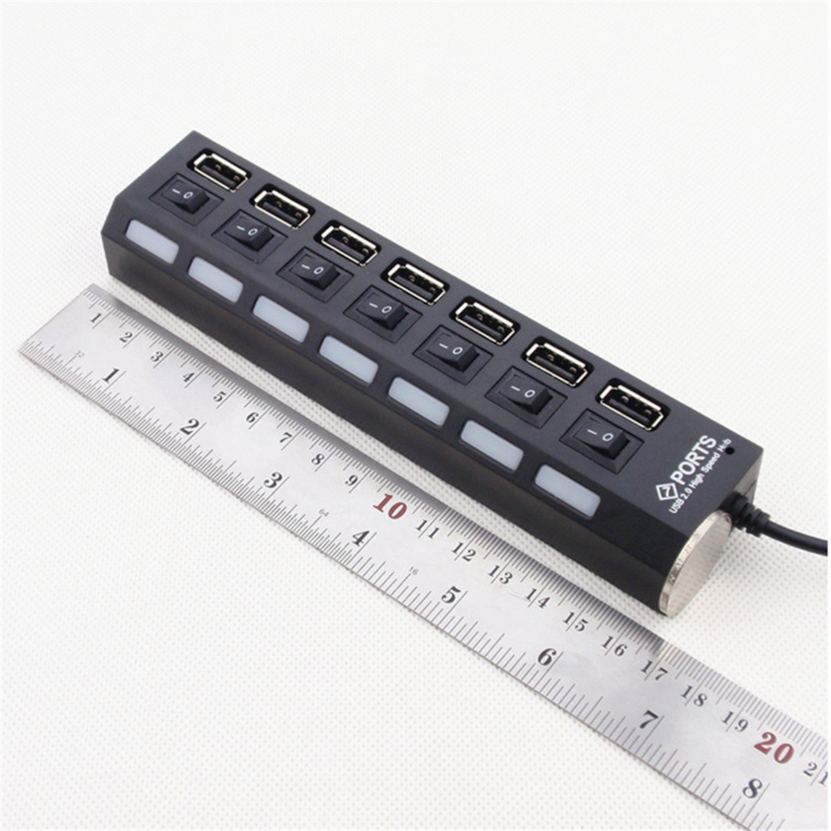 Schwarzer USB-Hub mit mehreren Anschlüssen. Ein Lineal liegt daneben.