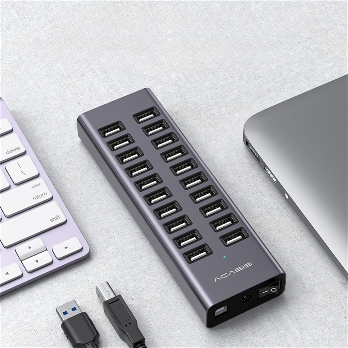 Ein grauer USB-Hub mit 16 Anschlüssen, Laptop und Tastatur auf dem Tisch.