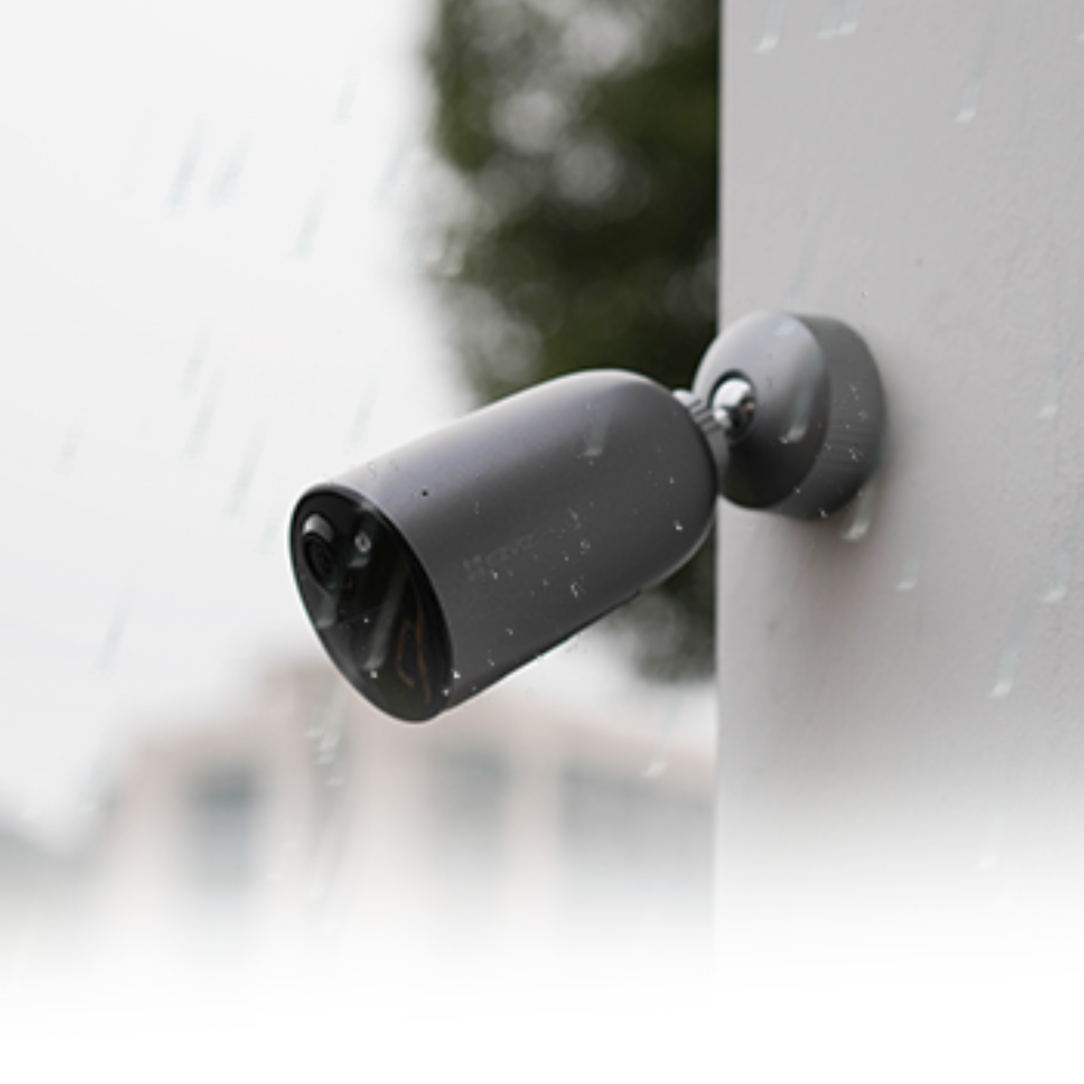 Czarna kamera monitoringu zamontowana na białej ścianie. Deszcz pada na kamerę.