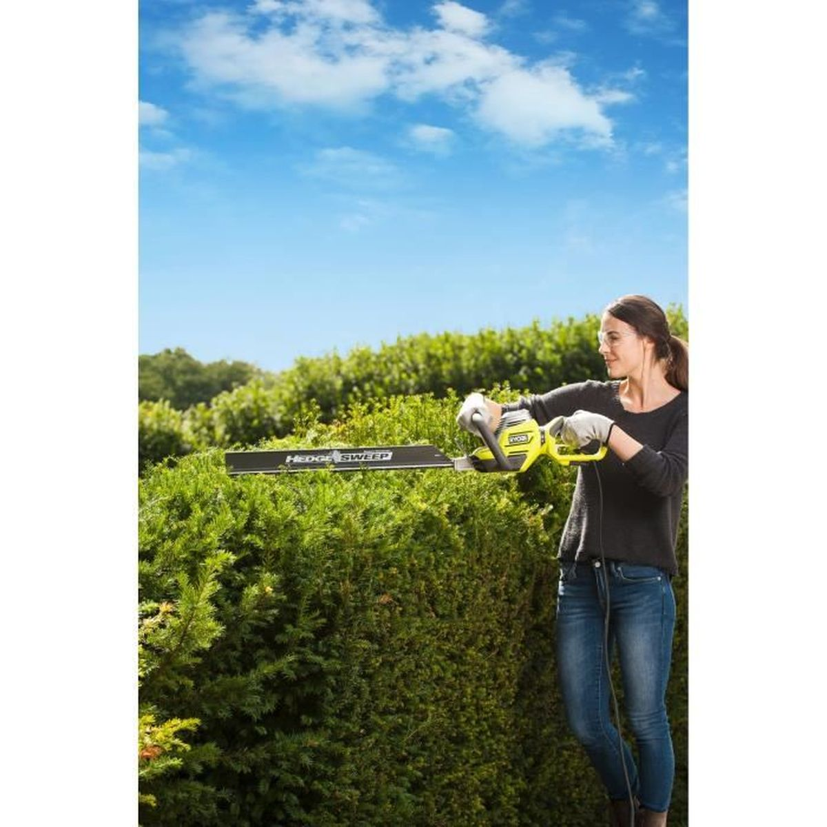 Frau benutzt Heckenschere an einer grünen Hecke unter blauem Himmel.