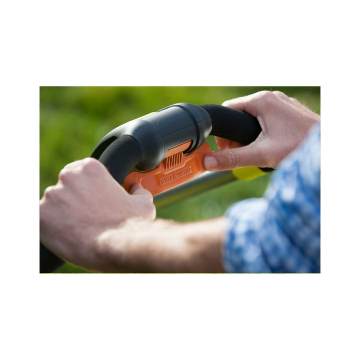 Nahaufnahme von Händen, die einen schwarz-orangenen Griff einer Maschine halten, grüner Gras-Hintergrund.