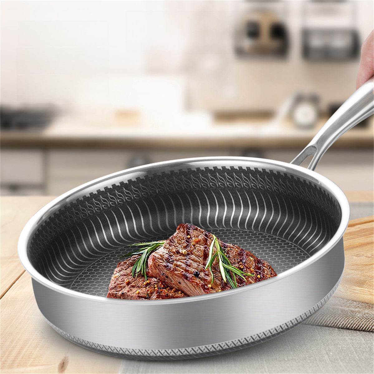 Eine Bratpfanne aus Edelstahl mit zwei Steaks und Rosmarin auf einer Holzoberfläche.
