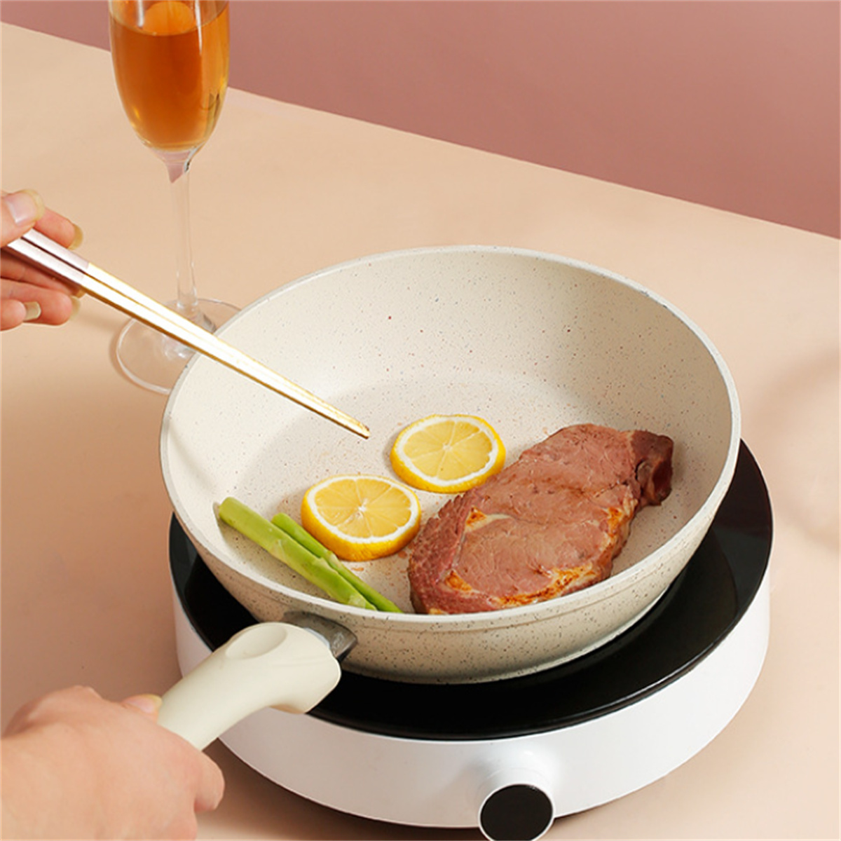 Steak, Zitronenscheiben, Spargel in einer Pfanne auf einem Elektroherd. Essstäbchen und Glas.