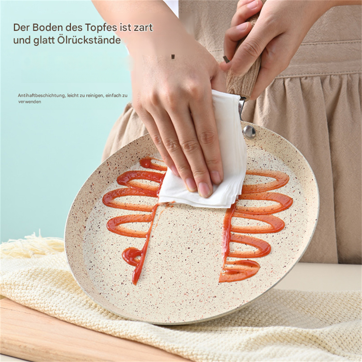 Hand reinigt Pfanne mit Ketchup. Weißes Tuch, beige Pfanne, rote Ketchup-Streifen.