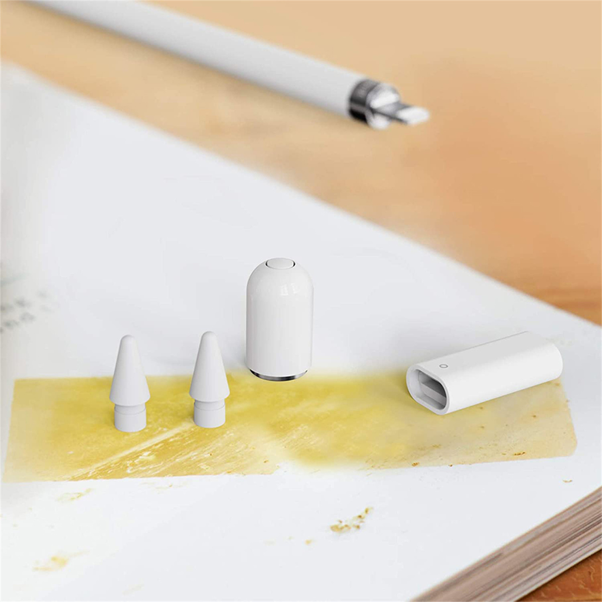 Weißer Apple Pencil und Zubehör auf einem Buch. Zubehör umfasst Spitzen und einen Ladeadapter.