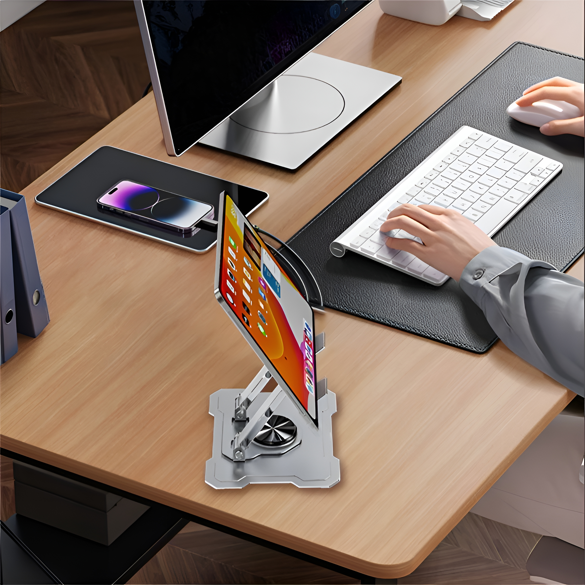 Tablet auf Ständer, Tastatur, Telefon und Monitor auf einem Holztisch. Hände tippen.