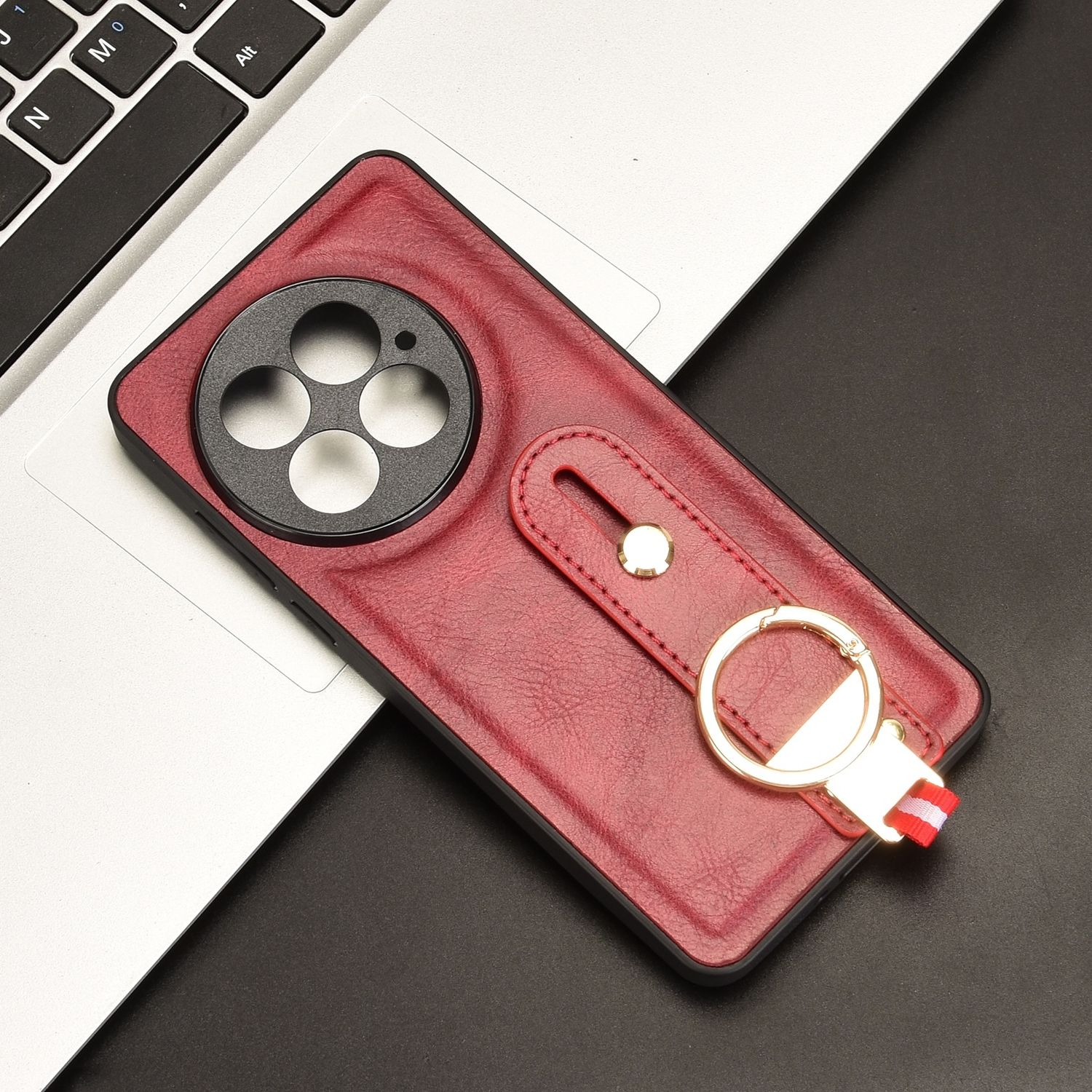 Rote Handyhülle mit Ringhalter und Kameraausschnitt. Laptop im Hintergrund.