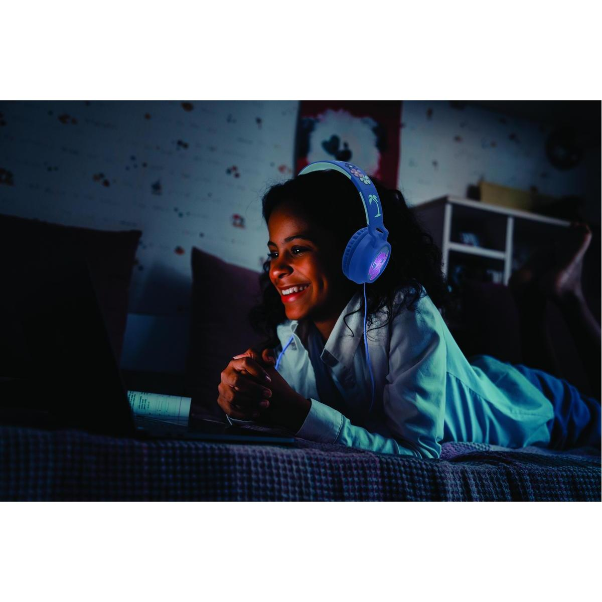 Dziewczyna w niebieskich słuchawkach patrzy na laptopa i uśmiecha się, leżąc na łóżku.