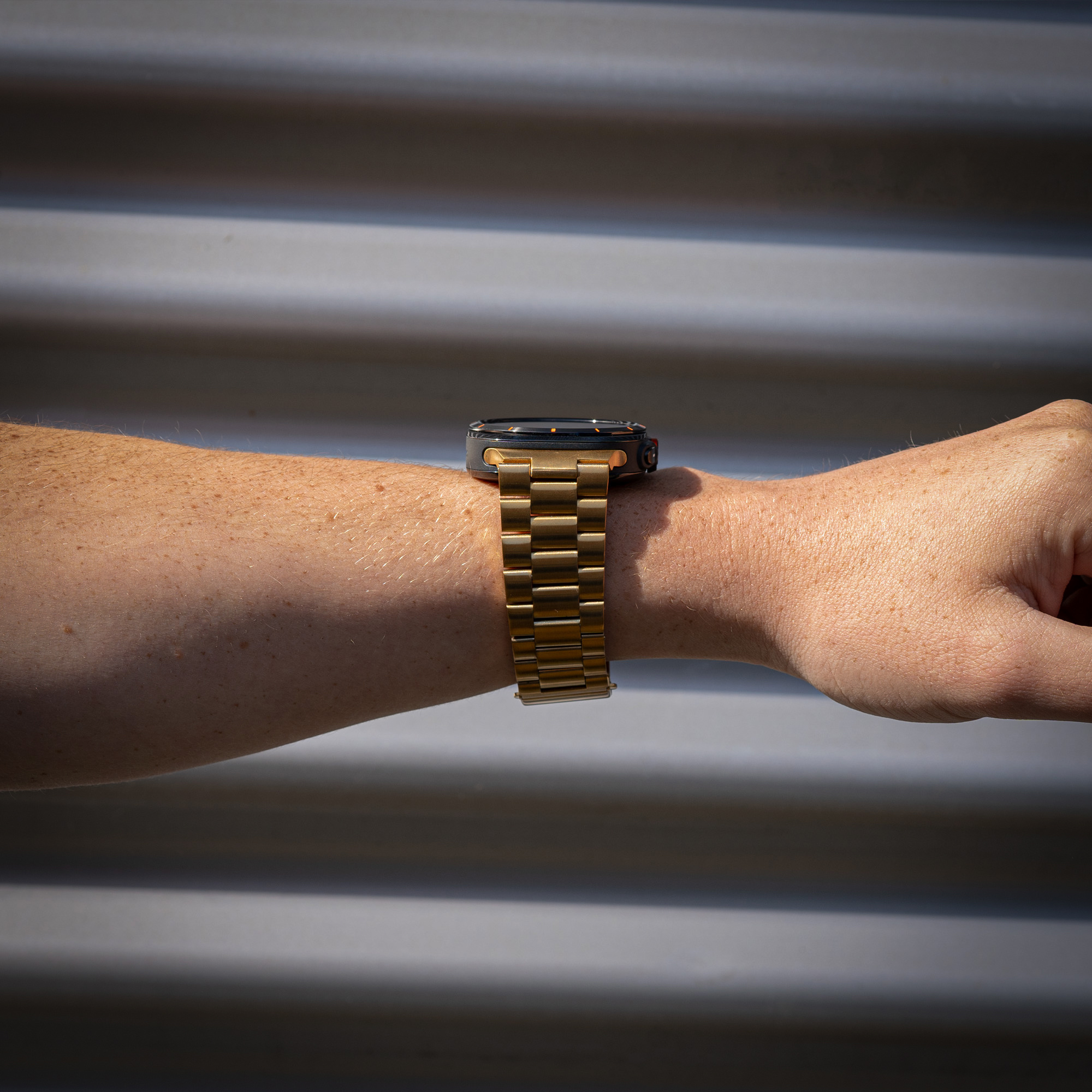 Das Handgelenk einer Person mit einer goldenen Uhr. Die Uhr hat ein goldenes Armband und ein dunkles Zifferblatt.