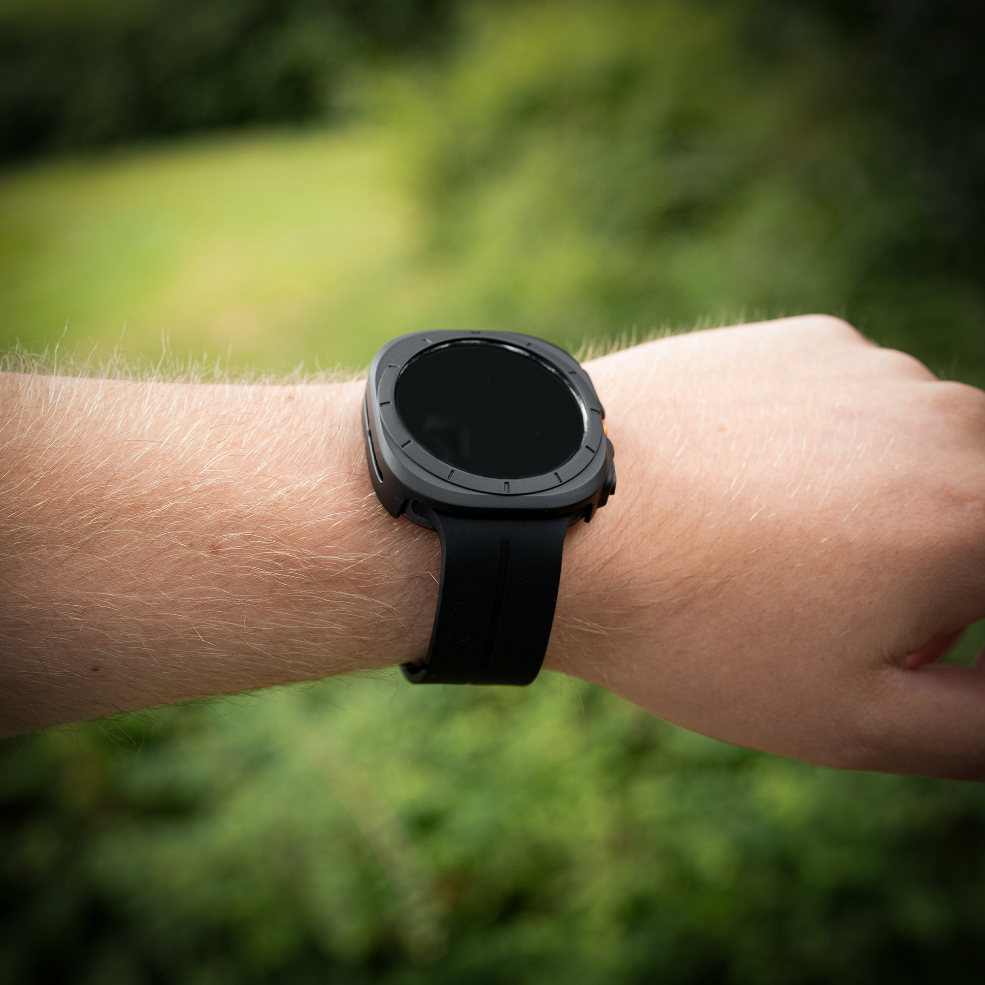 Schwarze Smartwatch am Handgelenk. Grünes Laub im Hintergrund.