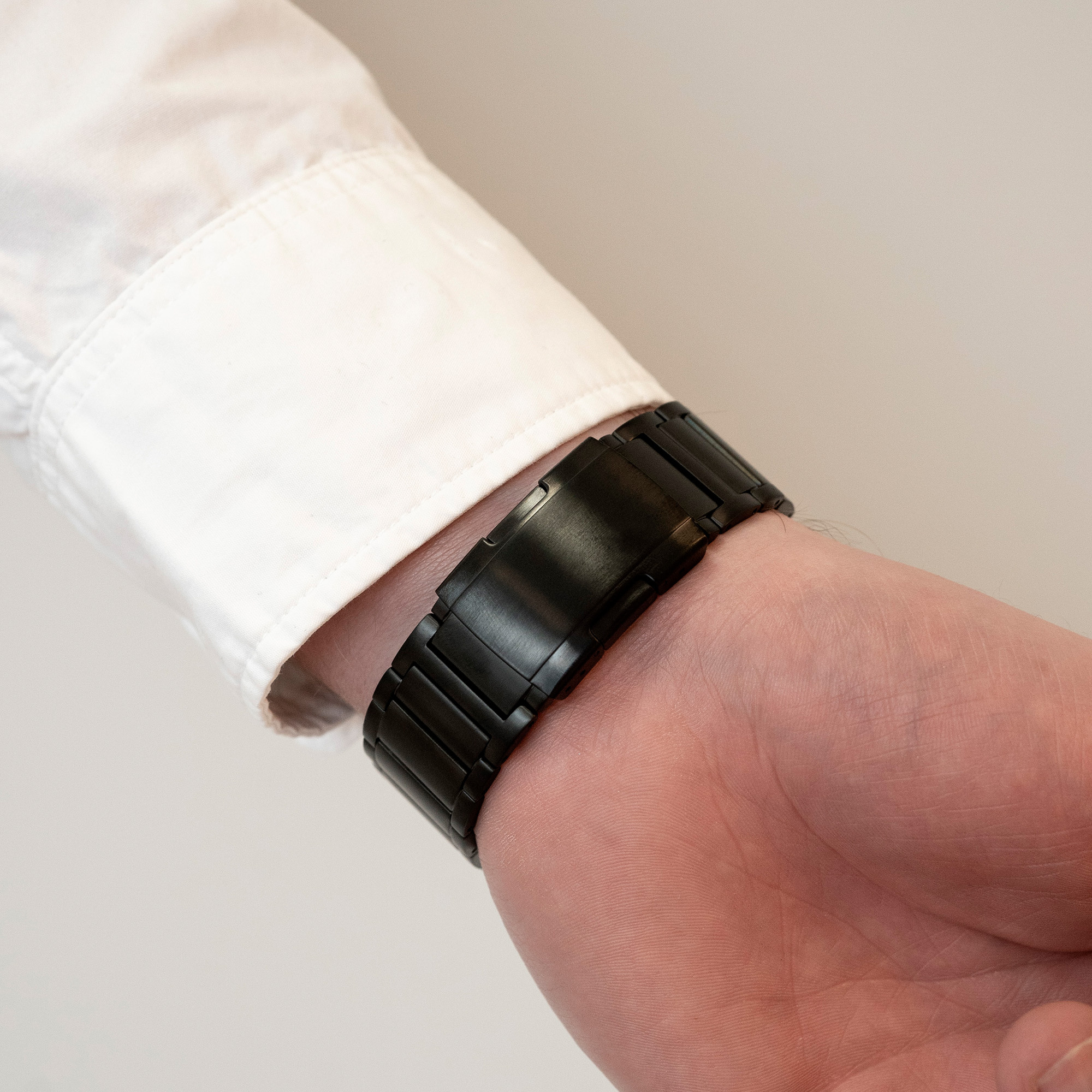 Das Handgelenk einer Person mit einem schwarzen Uhrenarmband. Die Person trägt ein weißes Hemd.