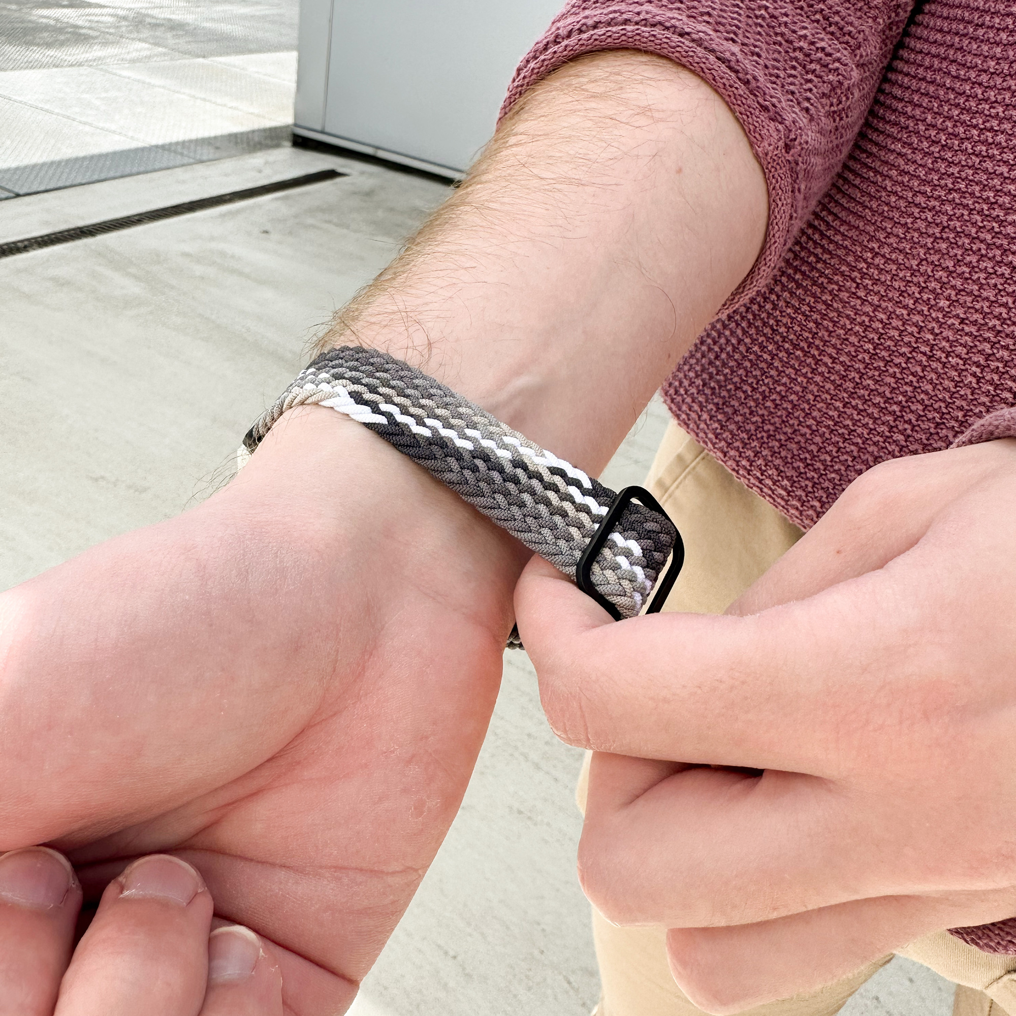 Das Handgelenk einer Person mit einem grau geflochtenen Uhrenarmband. Sie befestigen das Band.