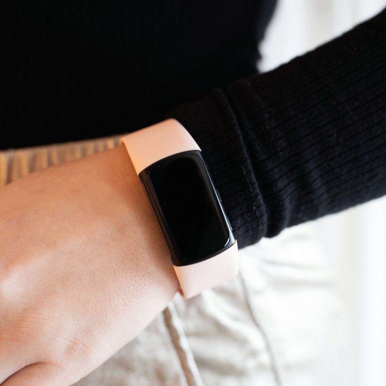 Rosa Fitness-Tracker am Handgelenk. Schwarzes Langarmshirt im Hintergrund.