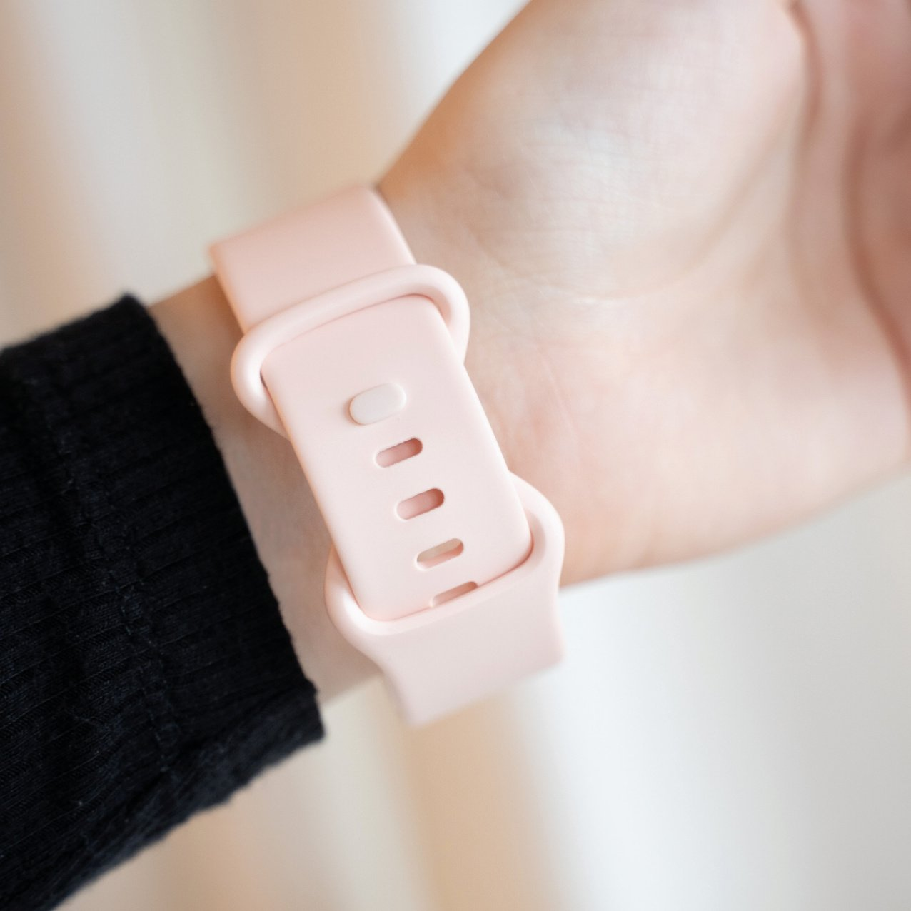 Ein rosa Armband an einem Handgelenk, mit einem schwarzen Ärmel im Hintergrund.