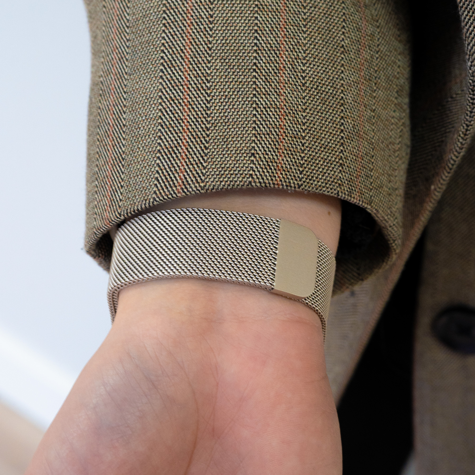 Ein silbernes Armband an einem Handgelenk, mit einer braunen Jacke im Hintergrund.