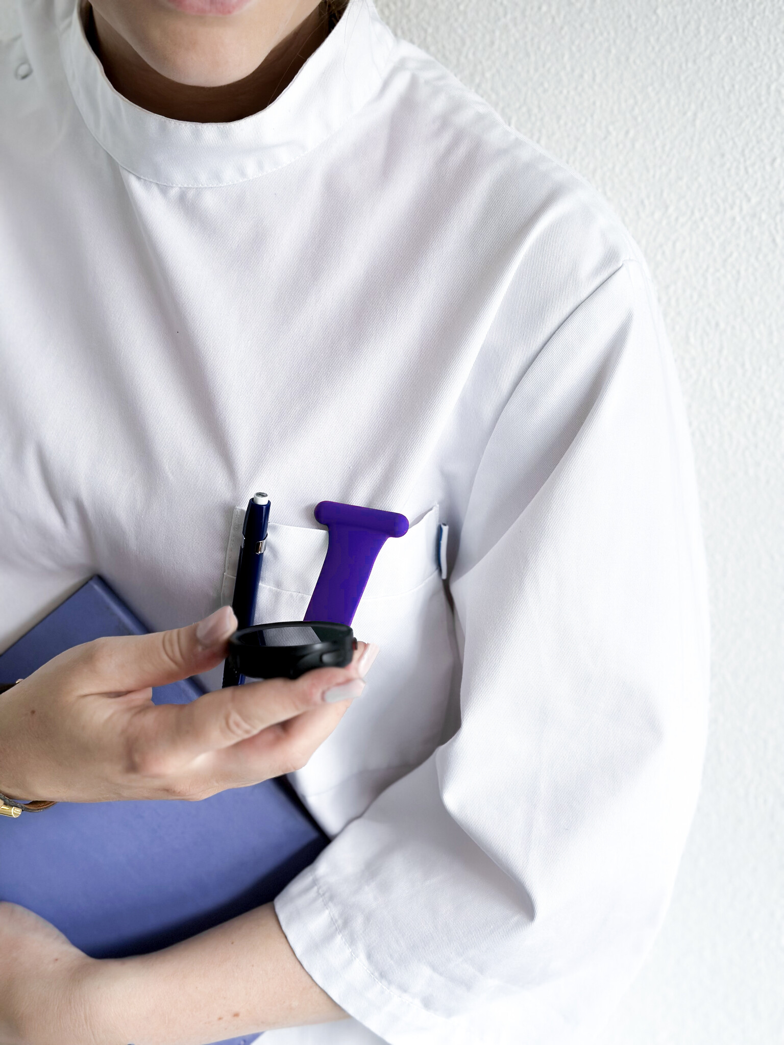 Eine Person in einem weißen Laborkittel hält einen blauen Ordner und eine Smartwatch vor weißem Hintergrund.