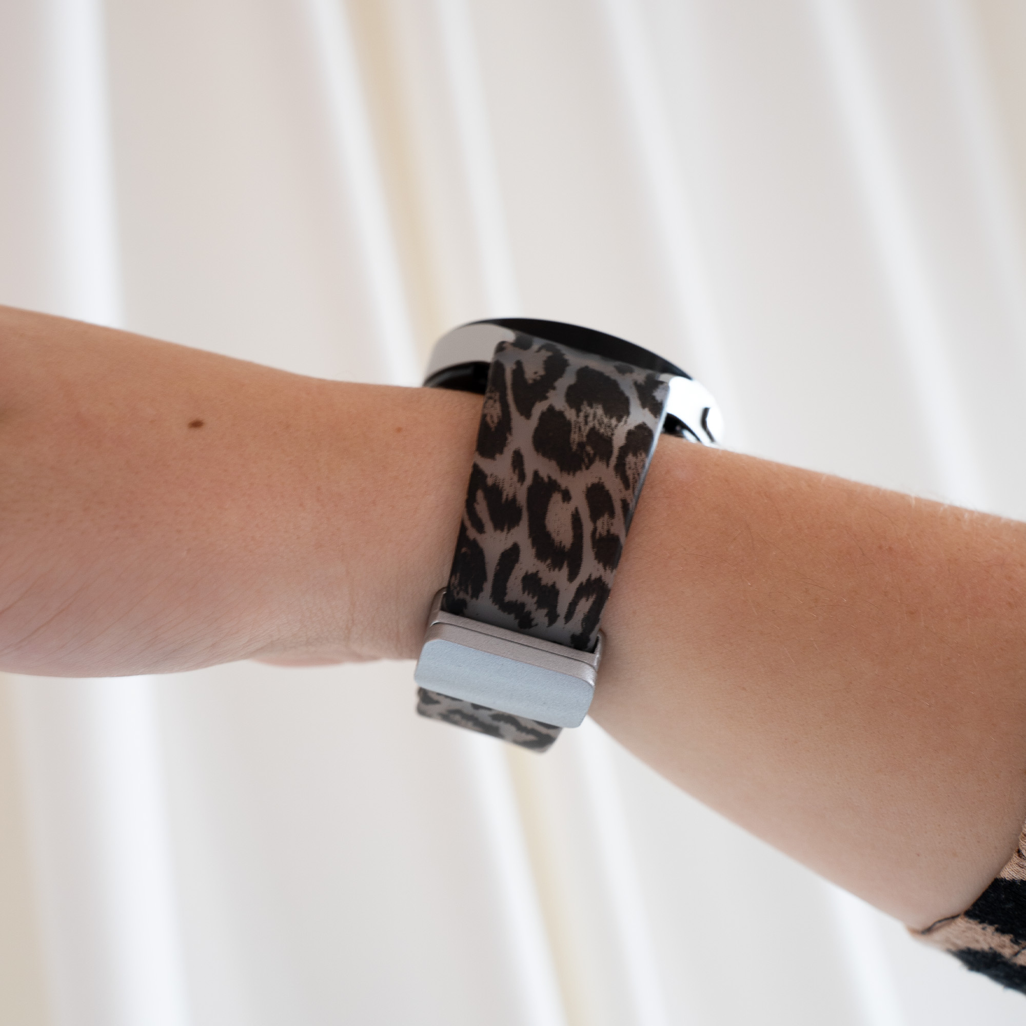 Das Handgelenk einer Person mit Leopardenmuster-Uhrenarmband und silberner Uhr.